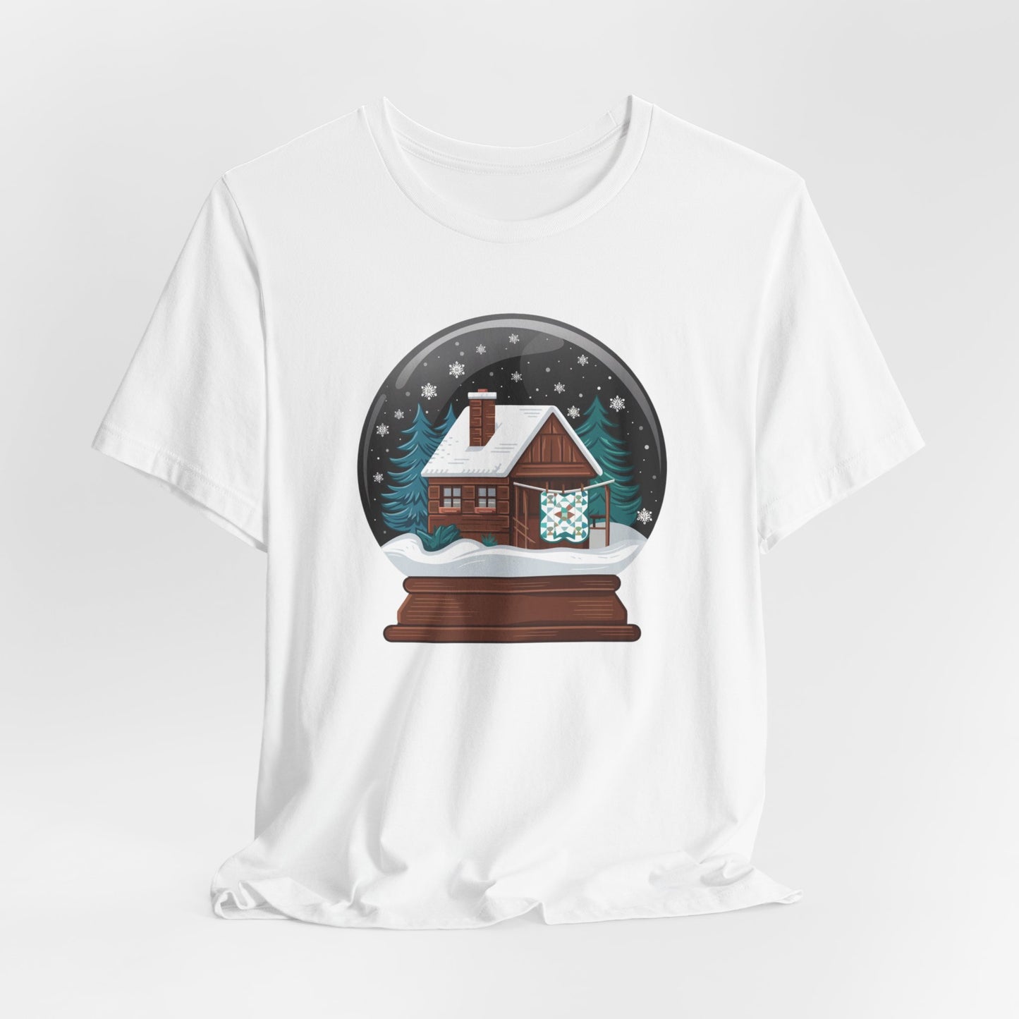 A White christmas quilting t-shirt featuring a cozy log cabin covered in snow, with a quilt hanging outside, set inside a snow globe with swirling snowflakes, blending quilting and holiday warmth.