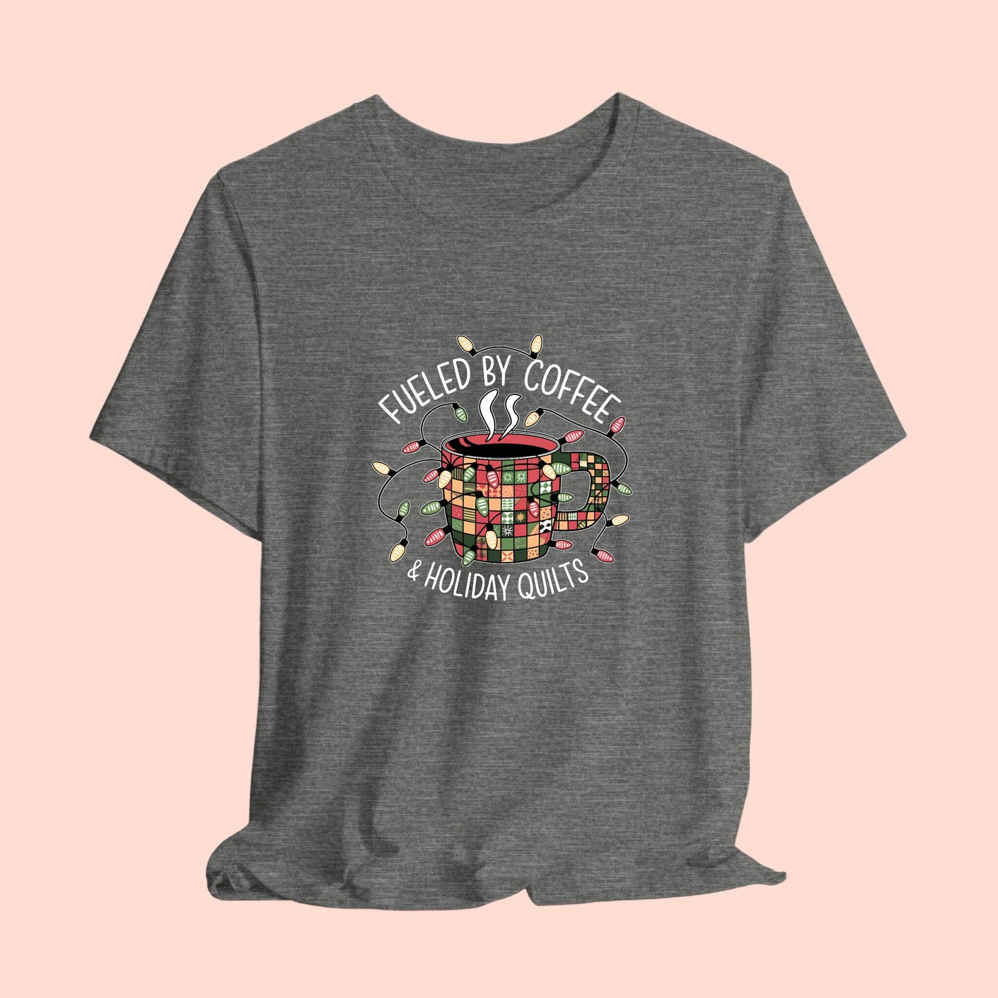 A christmas quilting t-shirt featuring a cozy coffee mug covered in patchwork quilt patterns, wrapped in festive holiday lights, with the phrase "Fueled by Coffee & Holiday Quilts" surrounding the design.