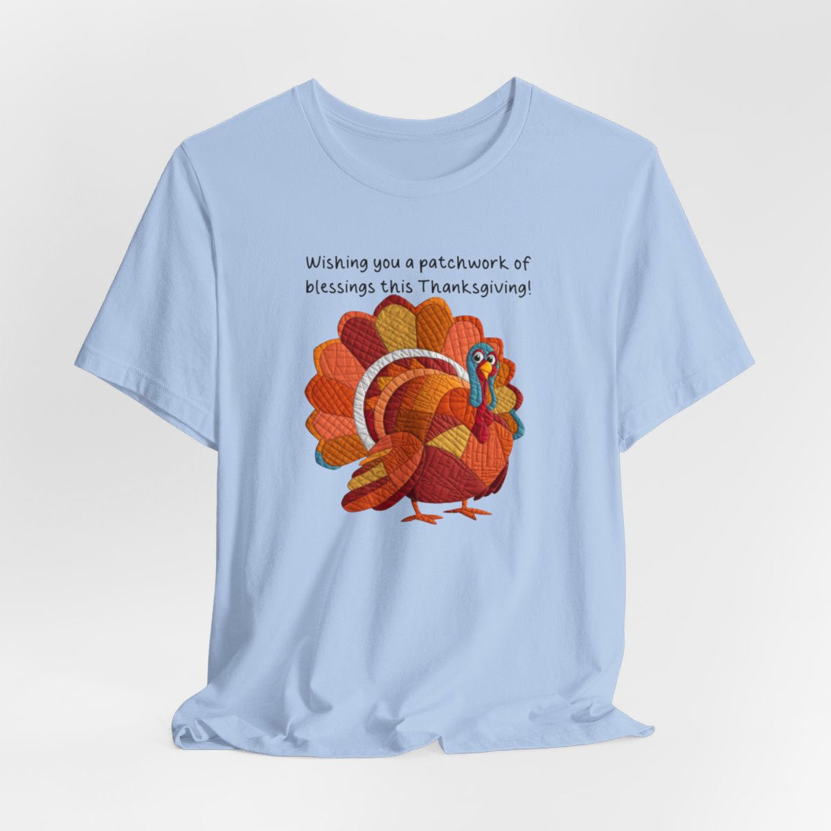 A thanksgiving quilting t-shirt featuring a quilted patchwork turkey in autumn colors with text "Wishing you a patchwork of blessings this Thanksgiving!" Turkey features various quilt patterns and textures in shades of orange, red, yellow, and blue. Whimsical, crafty holiday design perfect for quilting enthusiasts.