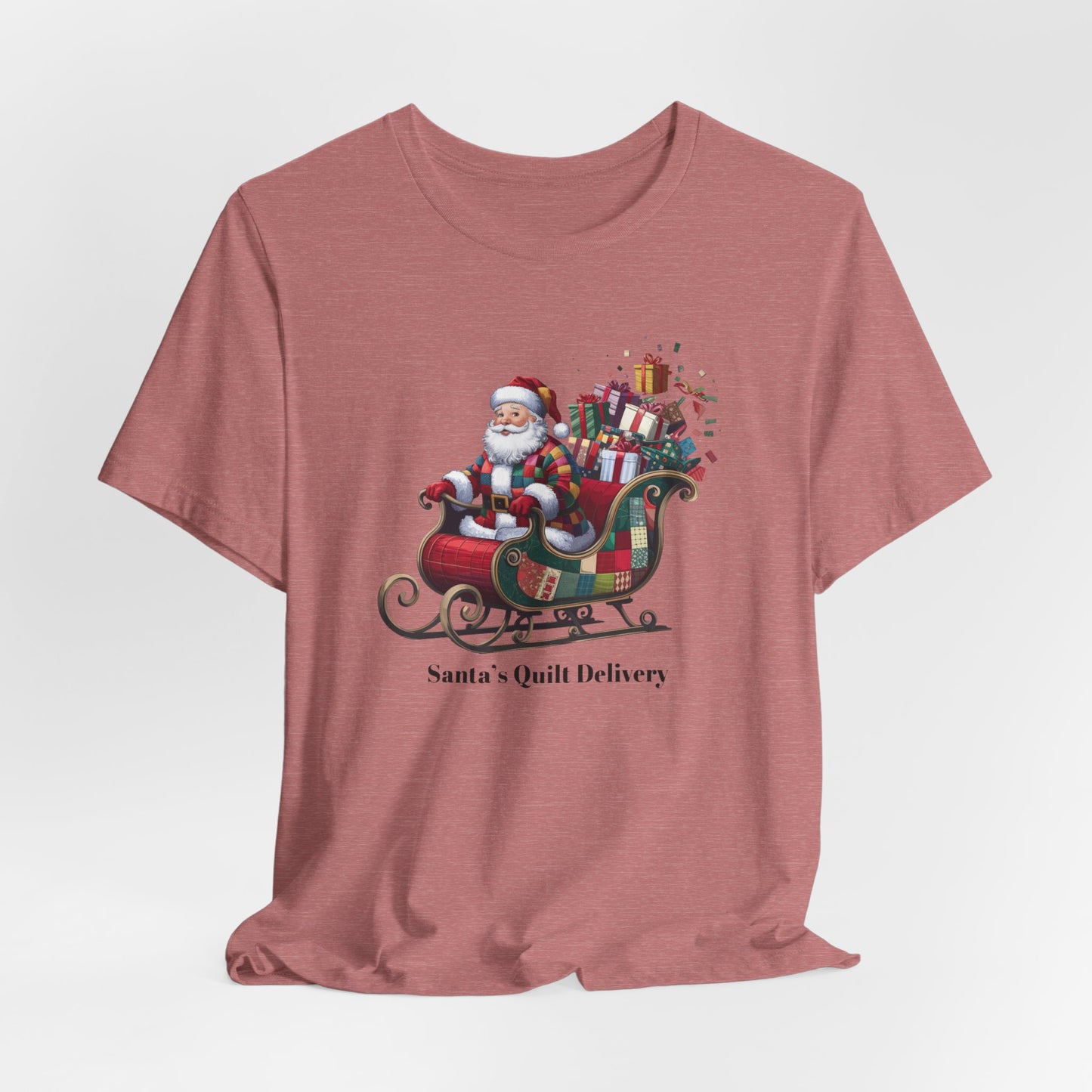 A Heather Mauve christmas quilting t-shirt featuring Santa Claus wearing a patchwork quilt coat, sitting in a sleigh filled with gifts and quilts, with the phrase "Santa's Quilt Delivery" below, combining holiday cheer and quilting fun.