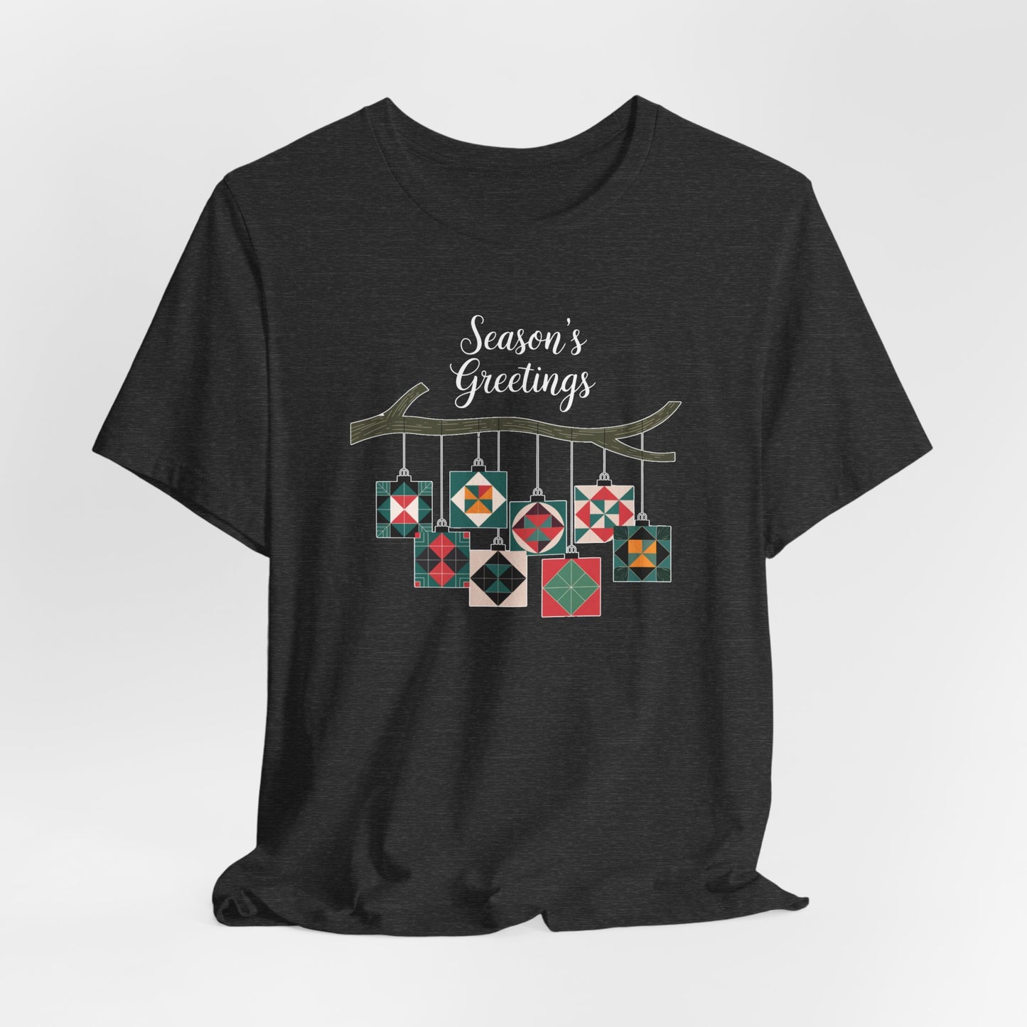 A Dark Grey Heather christmas quilting t-shirt featuring quilt block ornaments hanging from a branch, featuring the phrase "Season's Greetings" above. The ornaments showcase various quilting patterns to highlight the holiday quilting theme.
