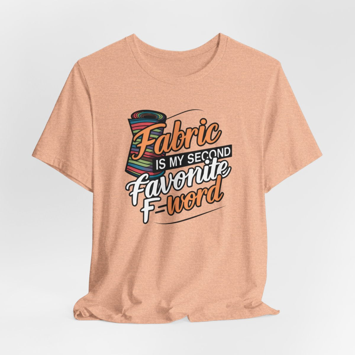 A Heather Peach T-Shirt with the phrase Fabric is My Second Favorite F-Word in a bold font next to a bolt of fabric