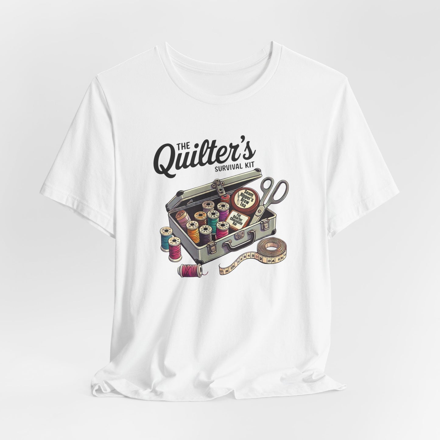 A White t-shirt featuring a whimsical illustration of a quilter’s survival kit with colorful thread spools, scissors, and a tape measure, perfect for sewing and quilting enthusiasts.