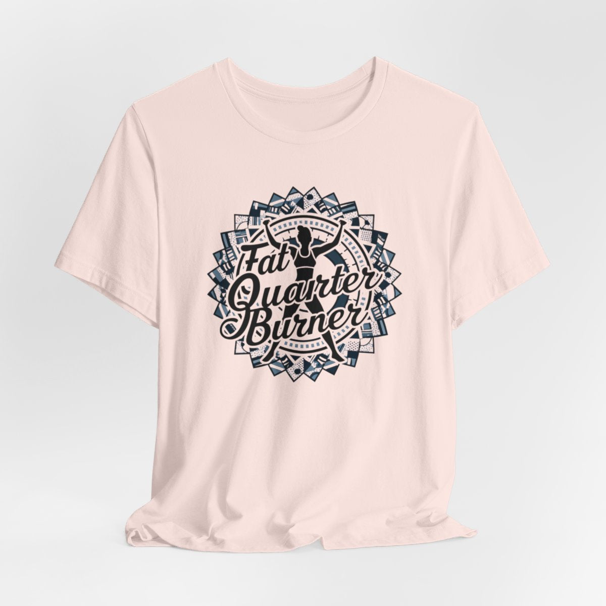 A Soft Pink T-Shirt featuring a patchwork border surrounding silhouette of woman lifting weights. Text reads "Fat Quarter Burner" in bold script.