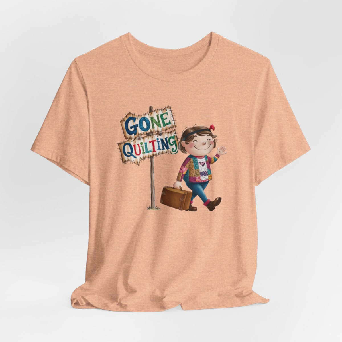 A Heather Peachfun quilting T-Shirt with a cartoon illustration of a smiling girl wearing a patchwork jacket, carrying a suitcase next to a wooden sign that reads "Gone Quilting" in colorful letters.