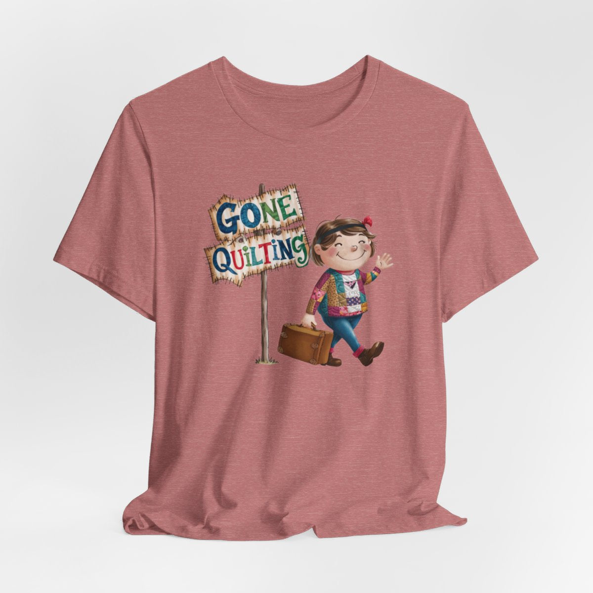 A Heather Mauvefun quilting T-Shirt with a cartoon illustration of a smiling girl wearing a patchwork jacket, carrying a suitcase next to a wooden sign that reads "Gone Quilting" in colorful letters.