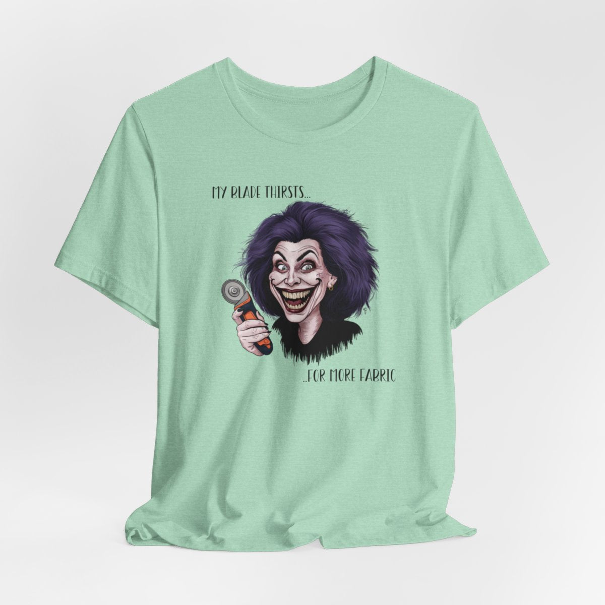 A Heather Mint T-shirt showing a cartoonish character with wild purple hair and an exaggerated grin, holding a rotary cutter. Text reads "My blade thirsts... for more fabric", humorously depicting a quilter's endless desire for new materials.