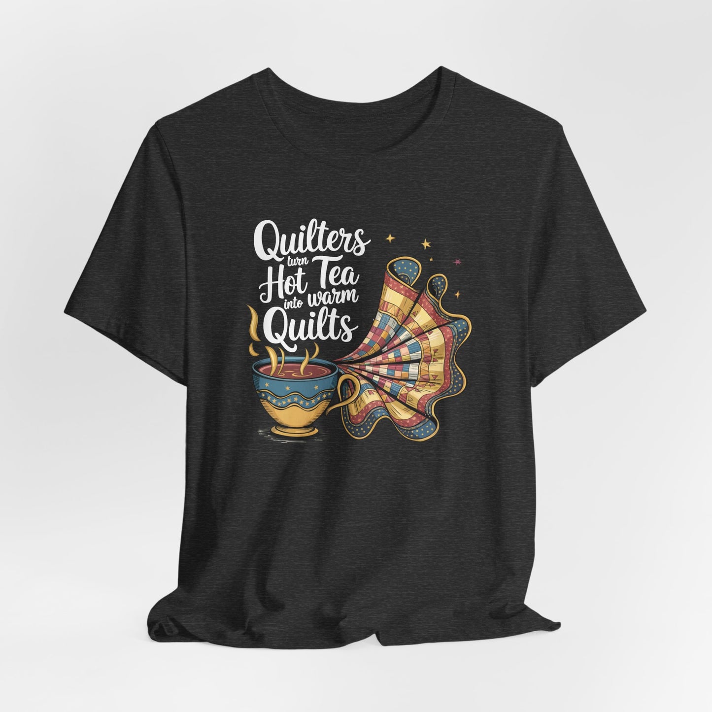 A Dark Grey Heather t-shirt with a whimsical design of a teacup transforming into a patchwork quilt, accompanied by the phrase 'Quilters turn hot tea into warm quilts.' Ideal for quilters and tea lovers