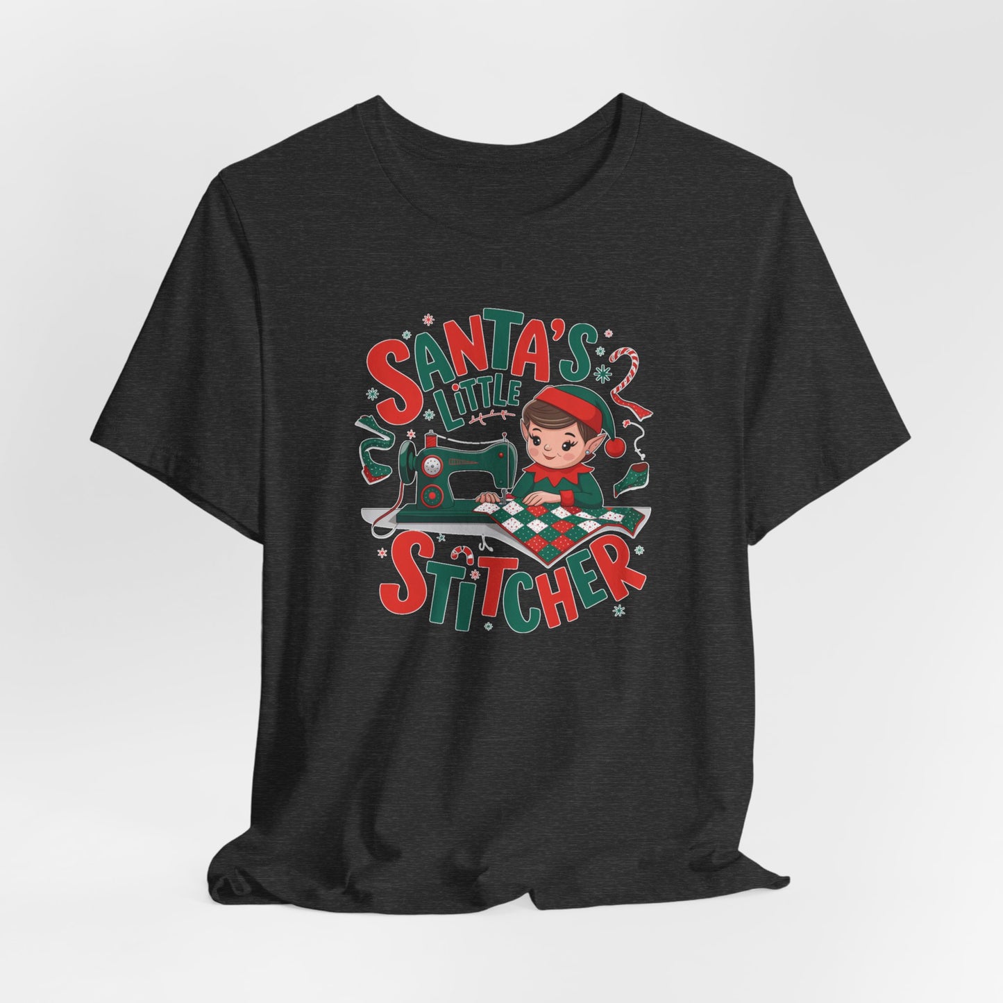 A Dark Grey Heather christmas quilting t-shirt featuring an adorable elf is sewing a festive patchwork quilt on a sewing machine, surrounded by holiday-themed decorations, with the phrase "Santa's Little Stitcher" above and below the design.