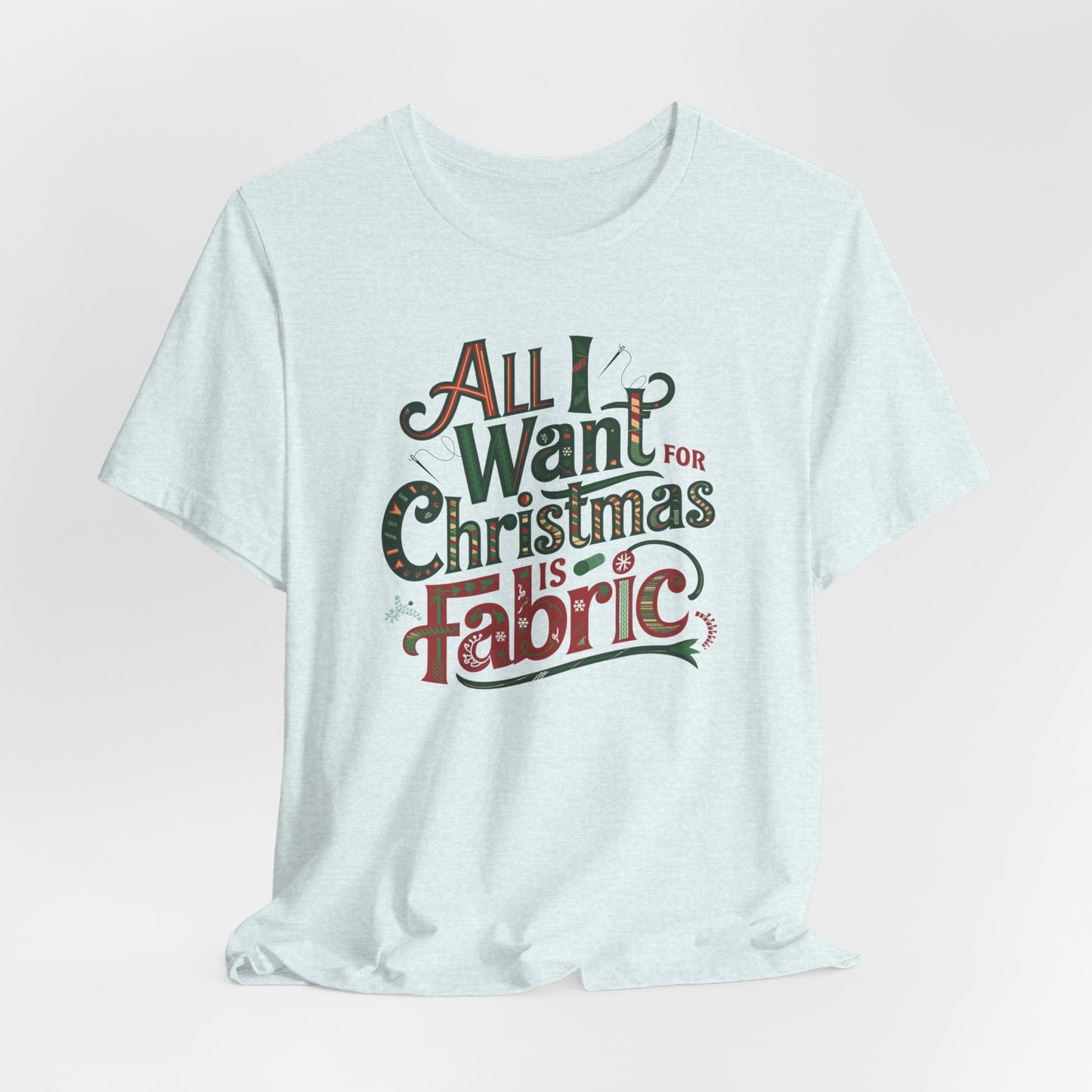 A Heather Ice Blue festive quilting christmas T-shirt featuring the phrase "All I Want for Christmas is Fabric," with fun sewing and quilting accents like needles and threads swirling around the text.