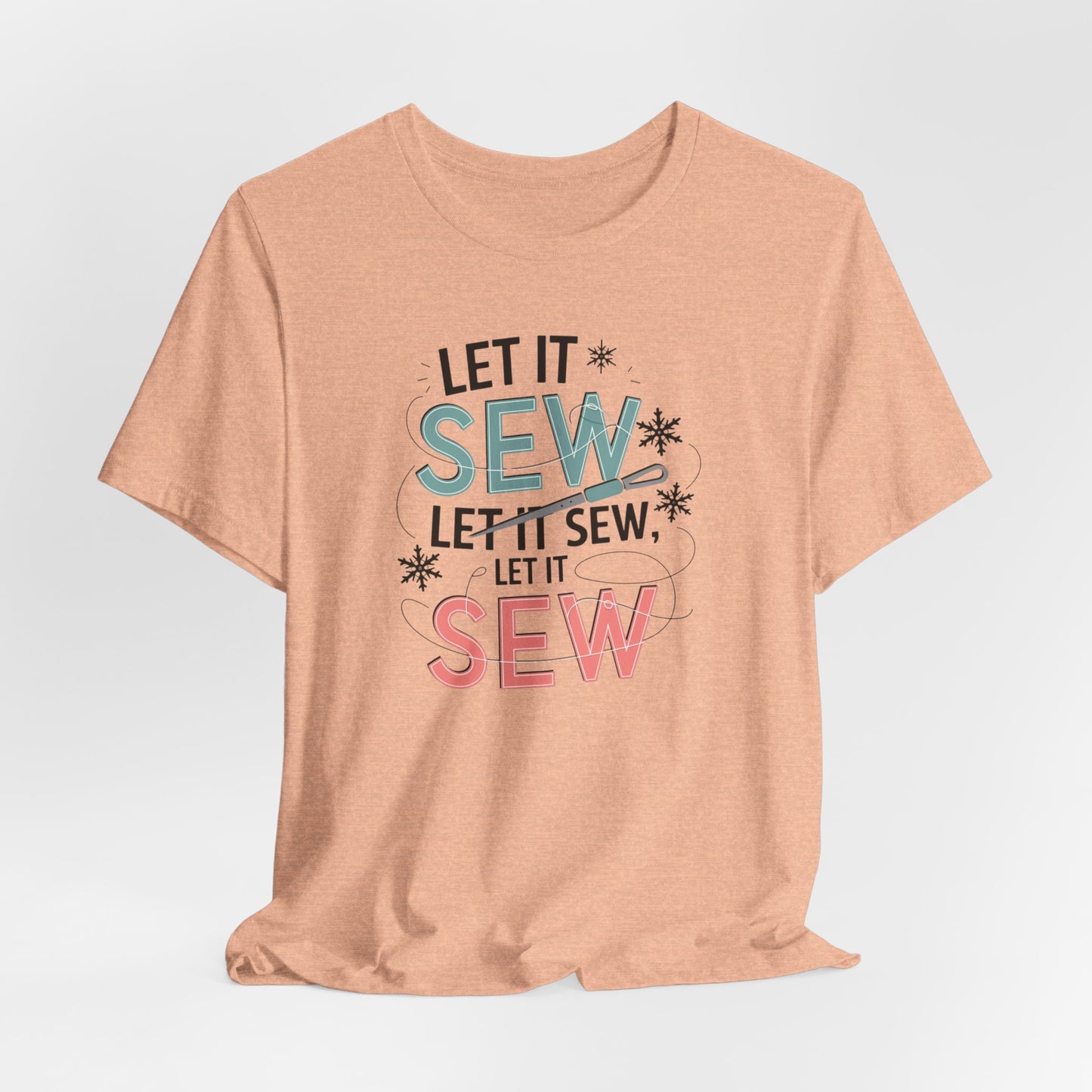 A Heather Peach christmas quilting t-shirt featuring the phrase "Let it Sew, Let it Sew, Let it Sew" featuring a needle and thread weaving through the letters, accented by snowflakes to bring out the holiday theme.