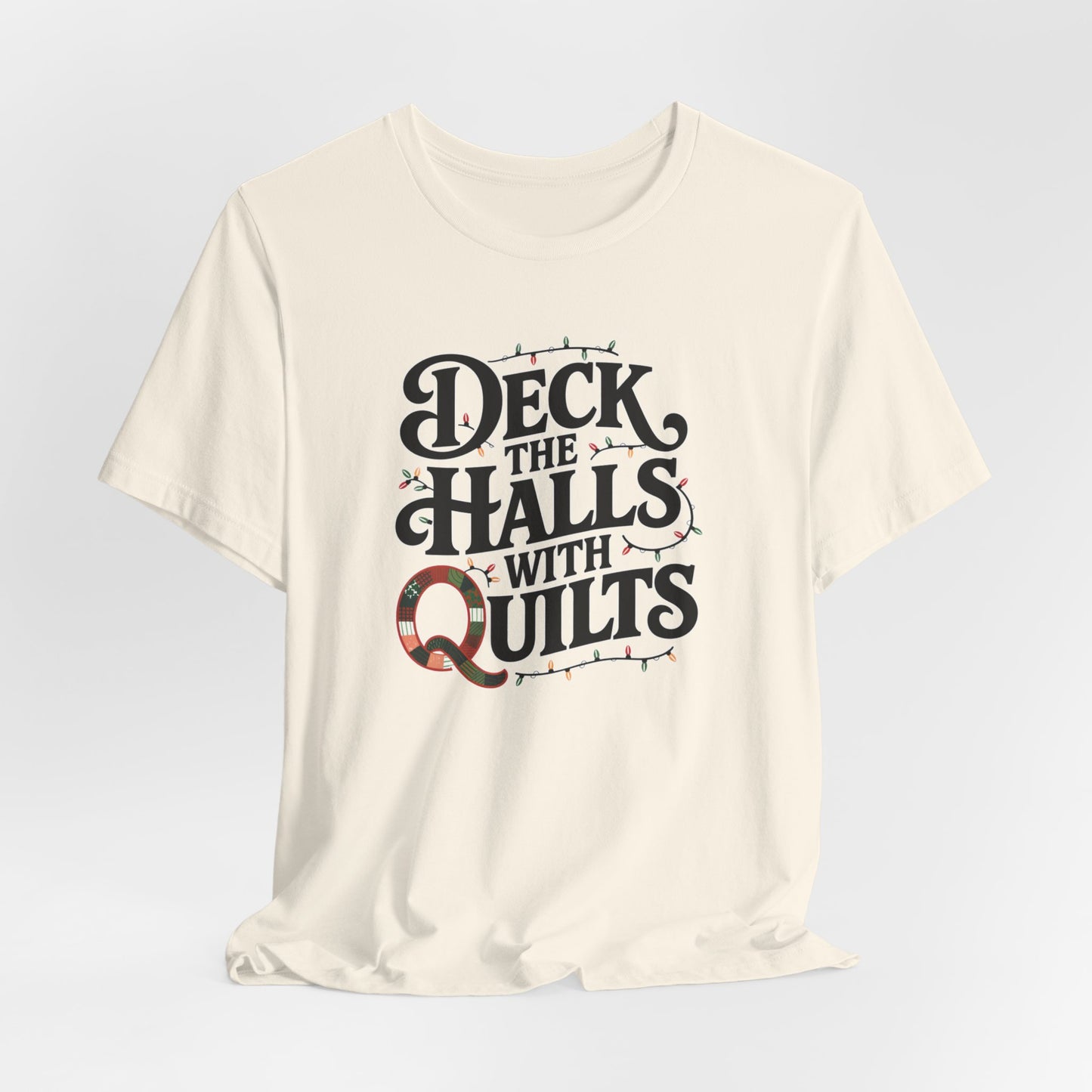 A Natural christmas quilting t-shirt featuring the phrase "Deck the Halls with Quilts," adorned with holiday lights and quilting-inspired elements, including a quilted 'Q' for a humorous touch.
