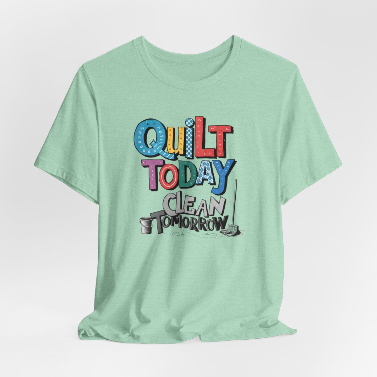 A Heather Mint funny quilting T-Shirt with the phrase Quilt Today, Clean Tomorrow in a bold and cheerful font with a broom off to the side