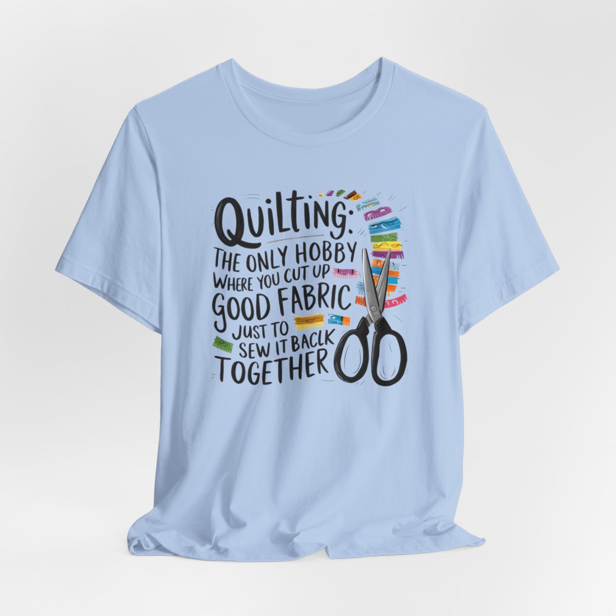 A Baby Blue Quilting-themed T-Shirt with text "Quilting: The Only Hobby Where You Cut Up Good Fabric Just to Sew it Back Together" surrounded by colorful fabric scraps and scissors.