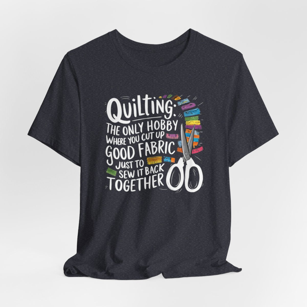 A Heather Navy Quilting-themed T-Shirt with text "Quilting: The Only Hobby Where You Cut Up Good Fabric Just to Sew it Back Together" surrounded by colorful fabric scraps and scissors.