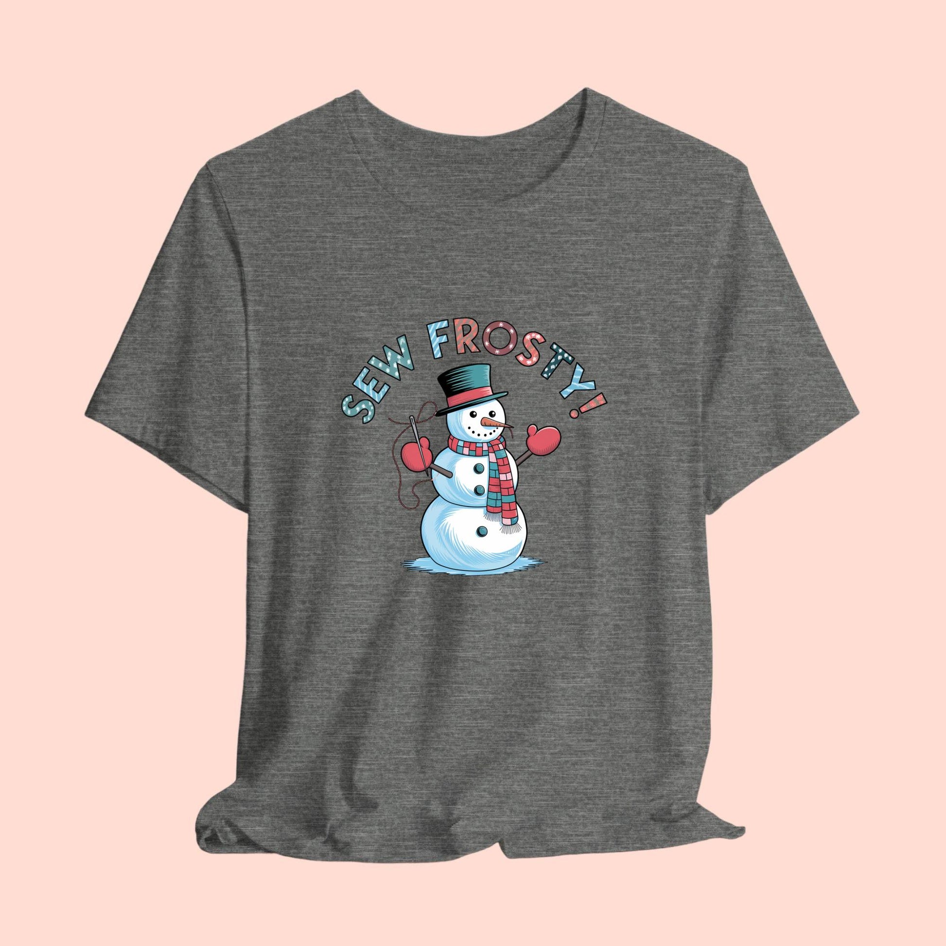 A christmas quilting t-shirt featuring cheerful snowman design holding a sewing needle, with the phrase "Sew Frosty" in playful, winter-themed lettering. The snowman is wearing a scarf and mittens, ready for holiday sewing fun.