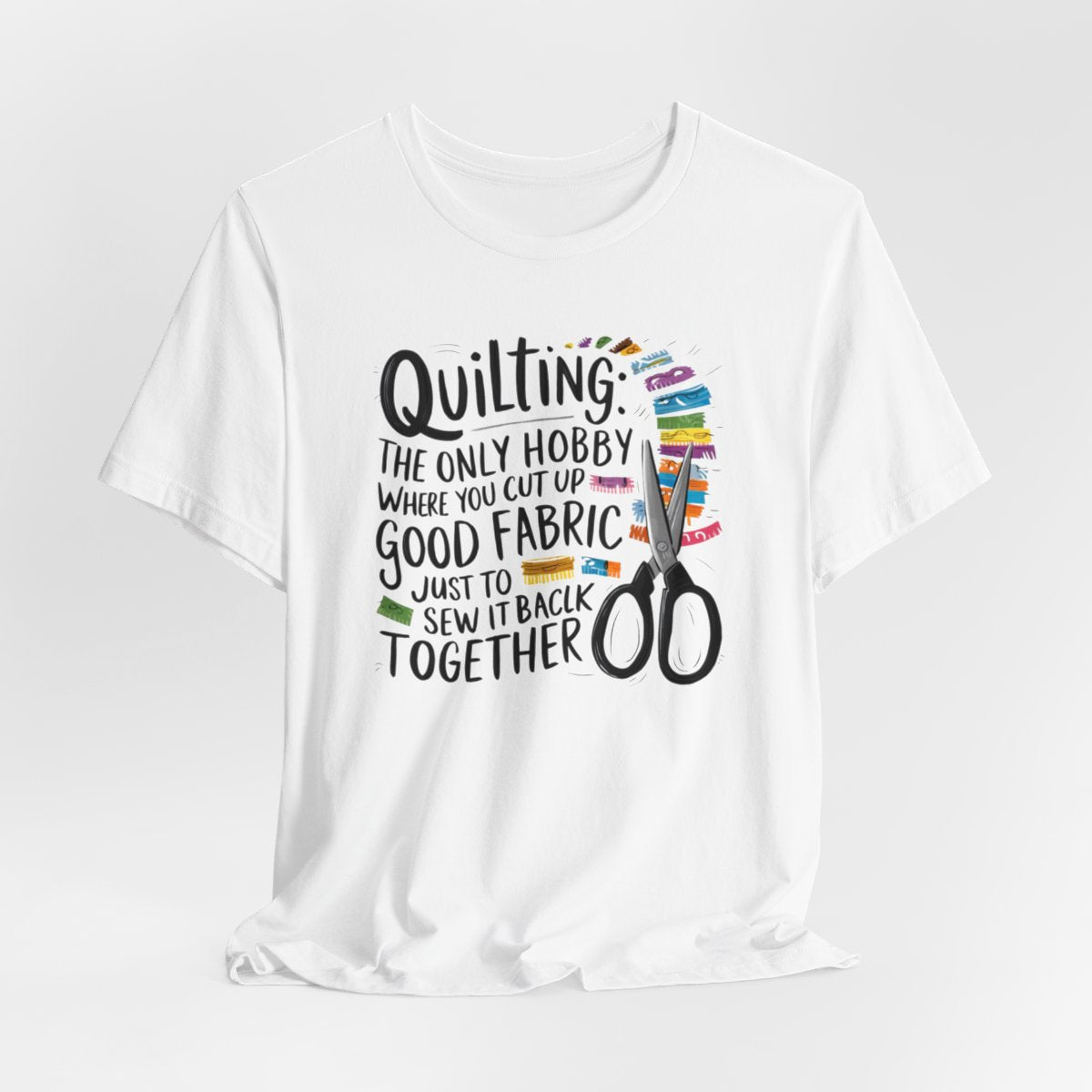 A White Quilting-themed T-Shirt with text "Quilting: The Only Hobby Where You Cut Up Good Fabric Just to Sew it Back Together" surrounded by colorful fabric scraps and scissors.