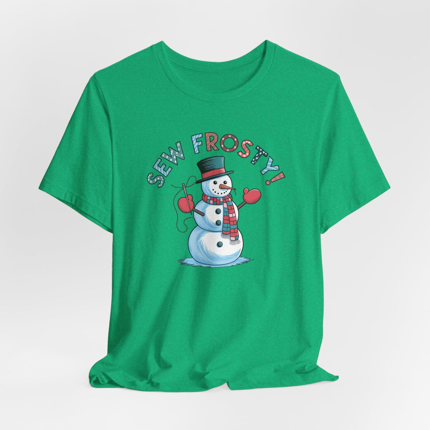 A Heather Kelly christmas quilting t-shirt featuring cheerful snowman design holding a sewing needle, with the phrase "Sew Frosty" in playful, winter-themed lettering. The snowman is wearing a scarf and mittens, ready for holiday sewing fun.