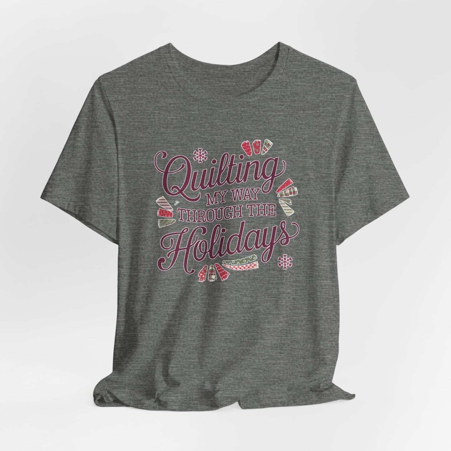 A Deep Heather playful holiday-themed t-shirt with the phrase "Quilting My Way Through the Holidays" surrounded by quilting-inspired decorations like fabric swatches and snowflakes.