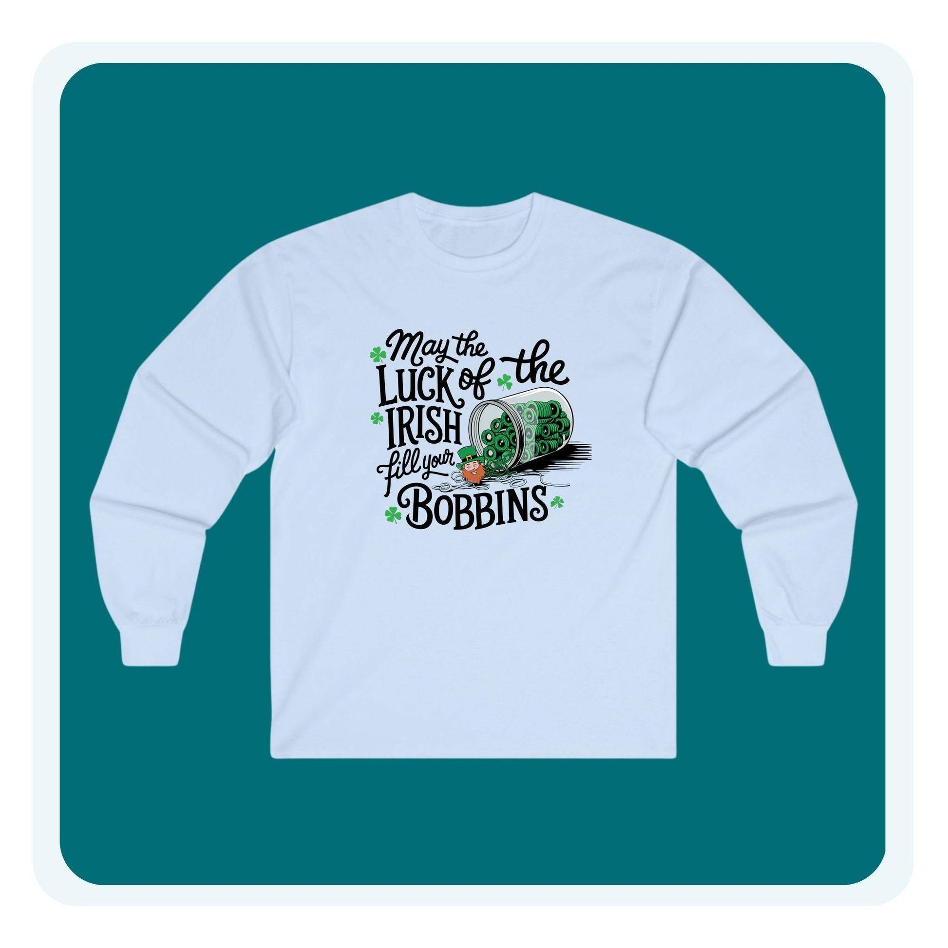A long-sleeve t-shirt featuring a festive design with shamrocks, a spool of green thread, and the phrase 'May the Luck of the Irish Fill Your Bobbins,' perfect for quilters celebrating St. Patrick’s Day.