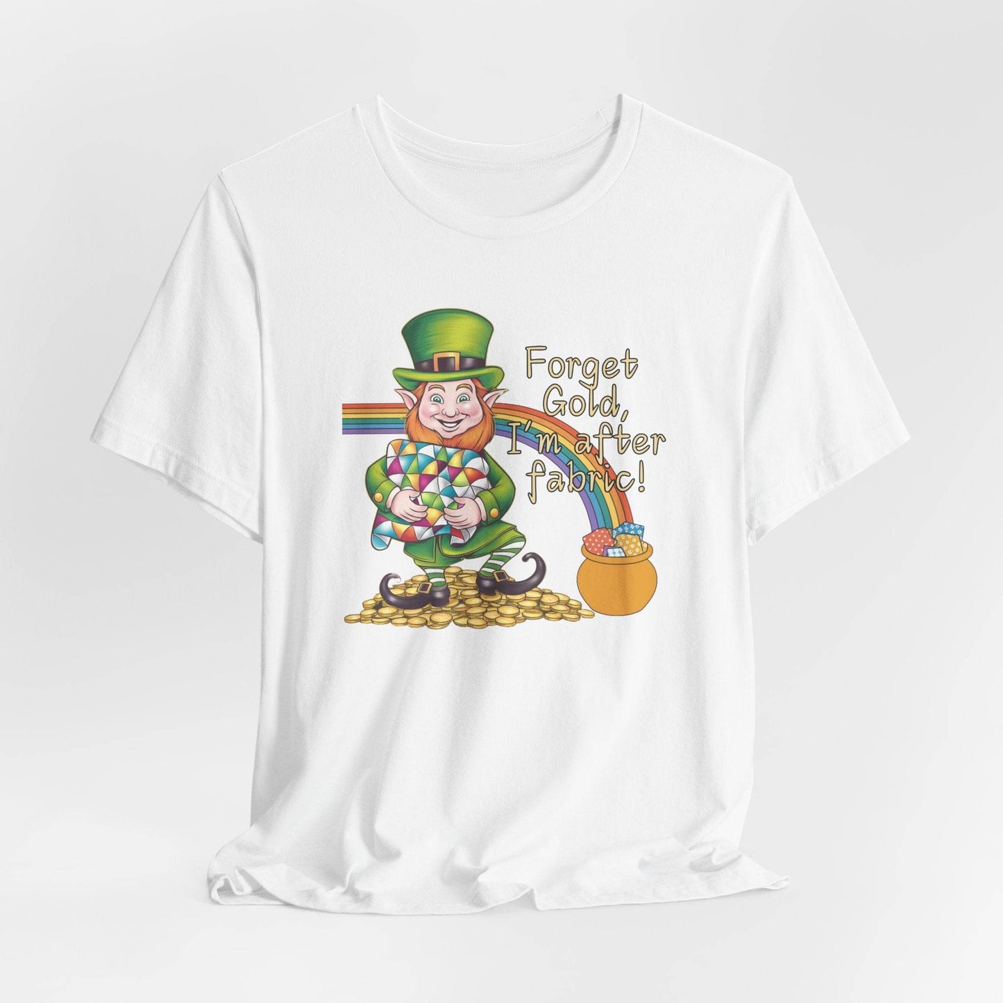 A White short-sleeve t-shirt featuring a cheerful leprechaun holding a quilt, sitting on gold coins, with a rainbow leading to a fabric-filled pot and the phrase 'Forget Gold, I’m After Fabric!' Perfect for quilters celebrating St. Patrick’s Day.