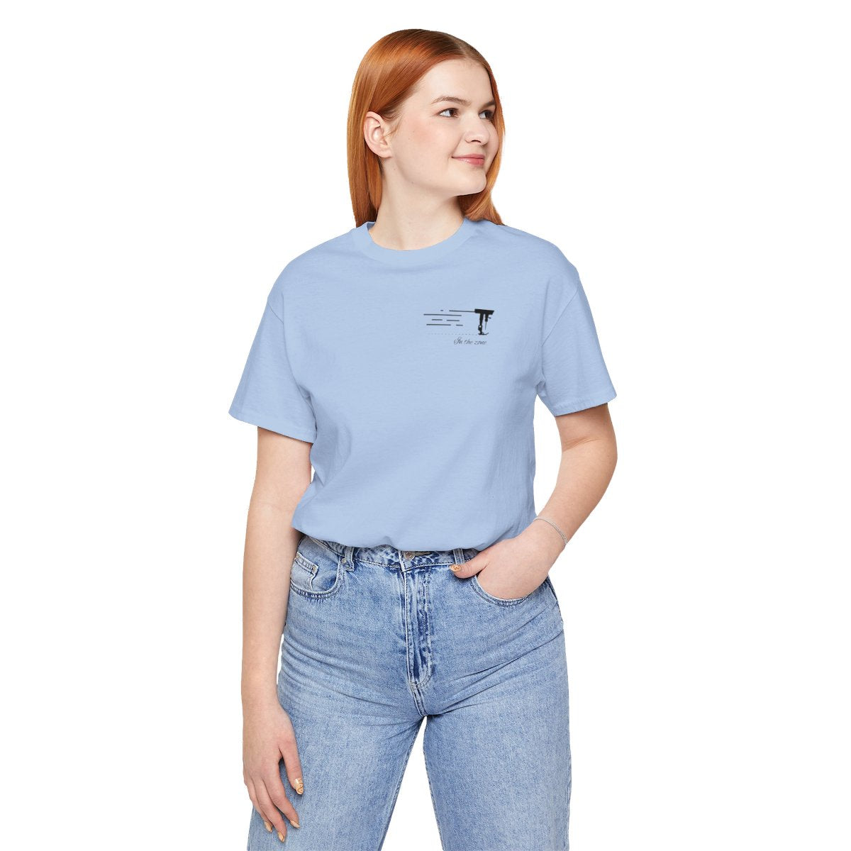 A Baby Blue T-shirt featuring a minimalist black silhouette of a sewing machine arm with motion lines. Below, the phrase "In the zone" is written in cursive script. The design conveys the focus and rhythm of quilting.