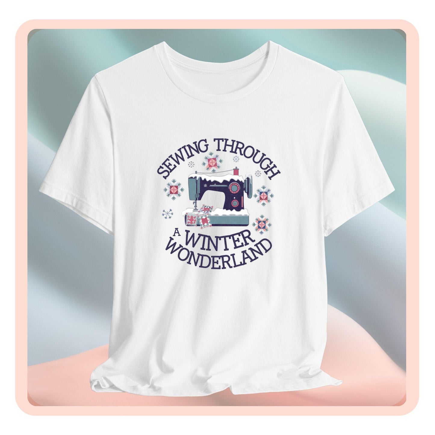 A winter quilting t-shirt featuring a sewing machine covered in snow, surrounded by quilted snowflakes, with the phrase "Sewing Through a Winter Wonderland" above and below the image.