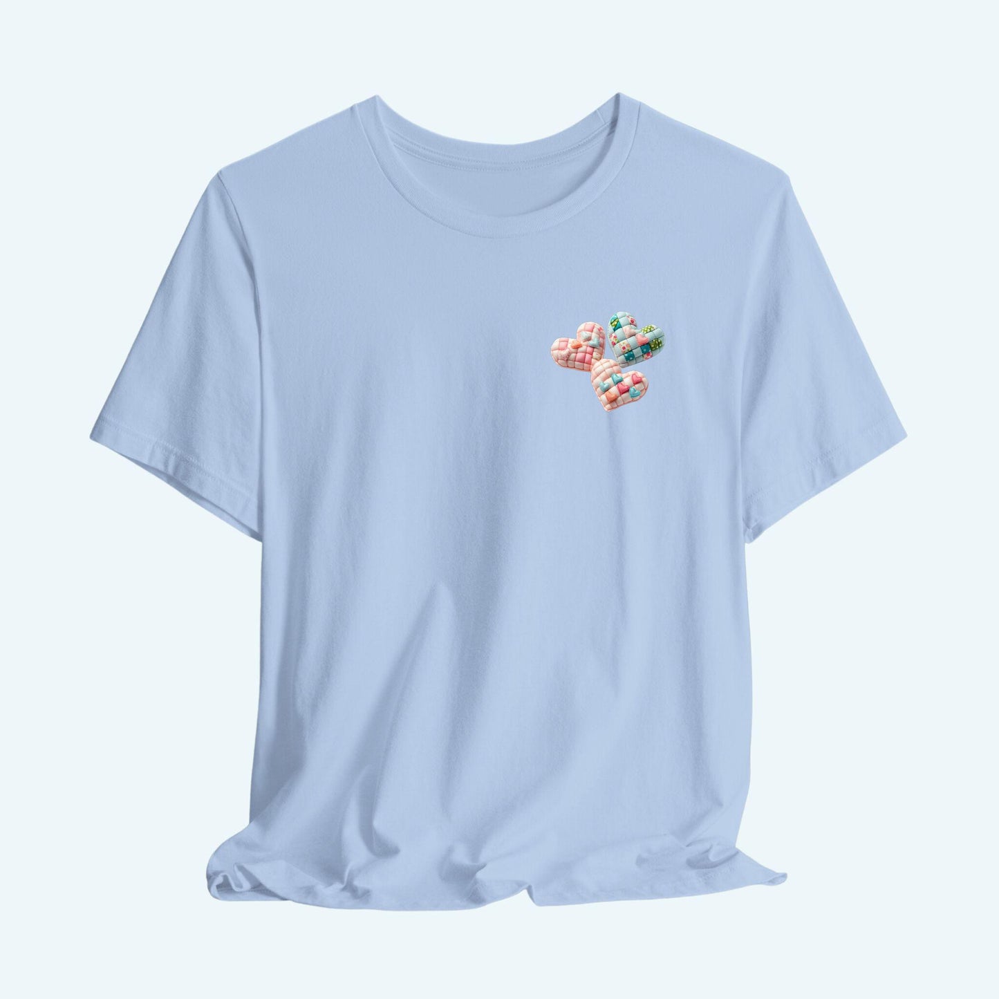 A Tshirt featuring Three heart-shaped quilted designs arranged together. Each heart features different quilting patterns and textures, including patchwork, floral prints, and tiny embroidered hearts. The hearts are in pastel shades of pink and blue, with white accents.