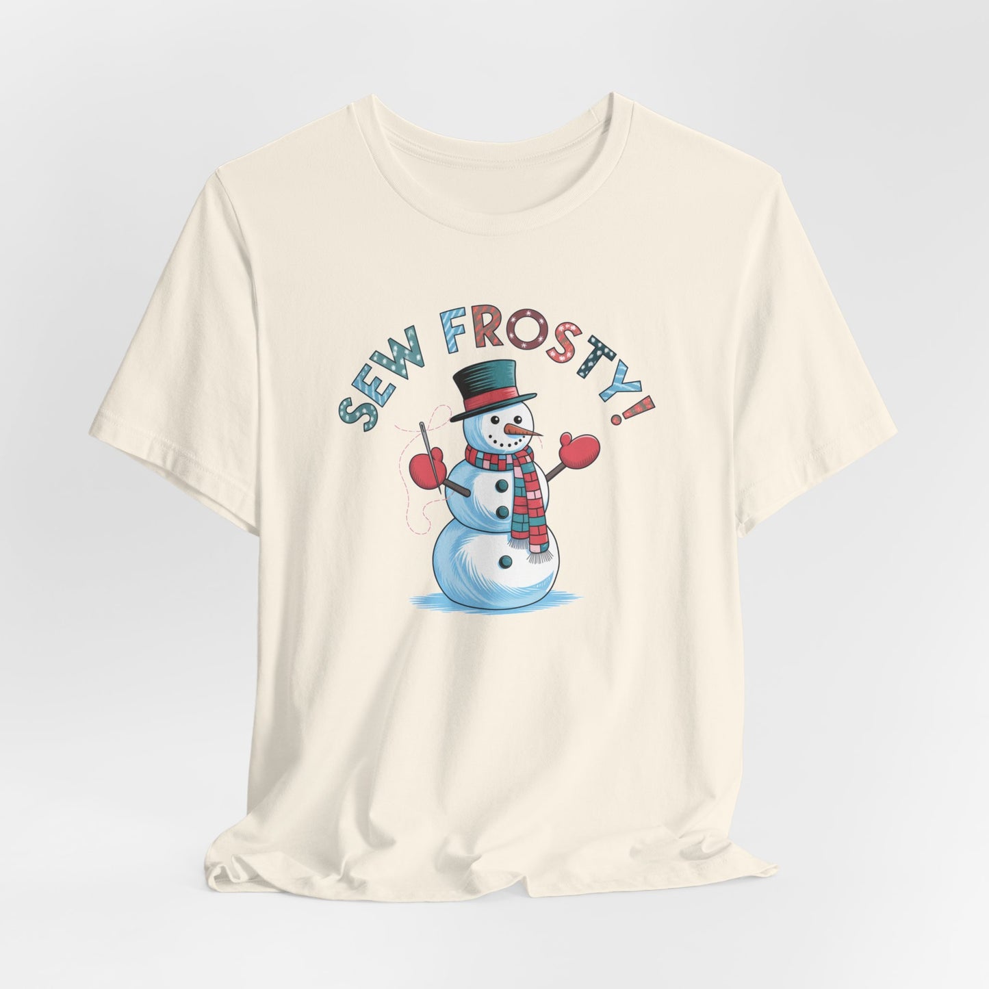 A Natural christmas quilting t-shirt featuring cheerful snowman design holding a sewing needle, with the phrase "Sew Frosty" in playful, winter-themed lettering. The snowman is wearing a scarf and mittens, ready for holiday sewing fun.