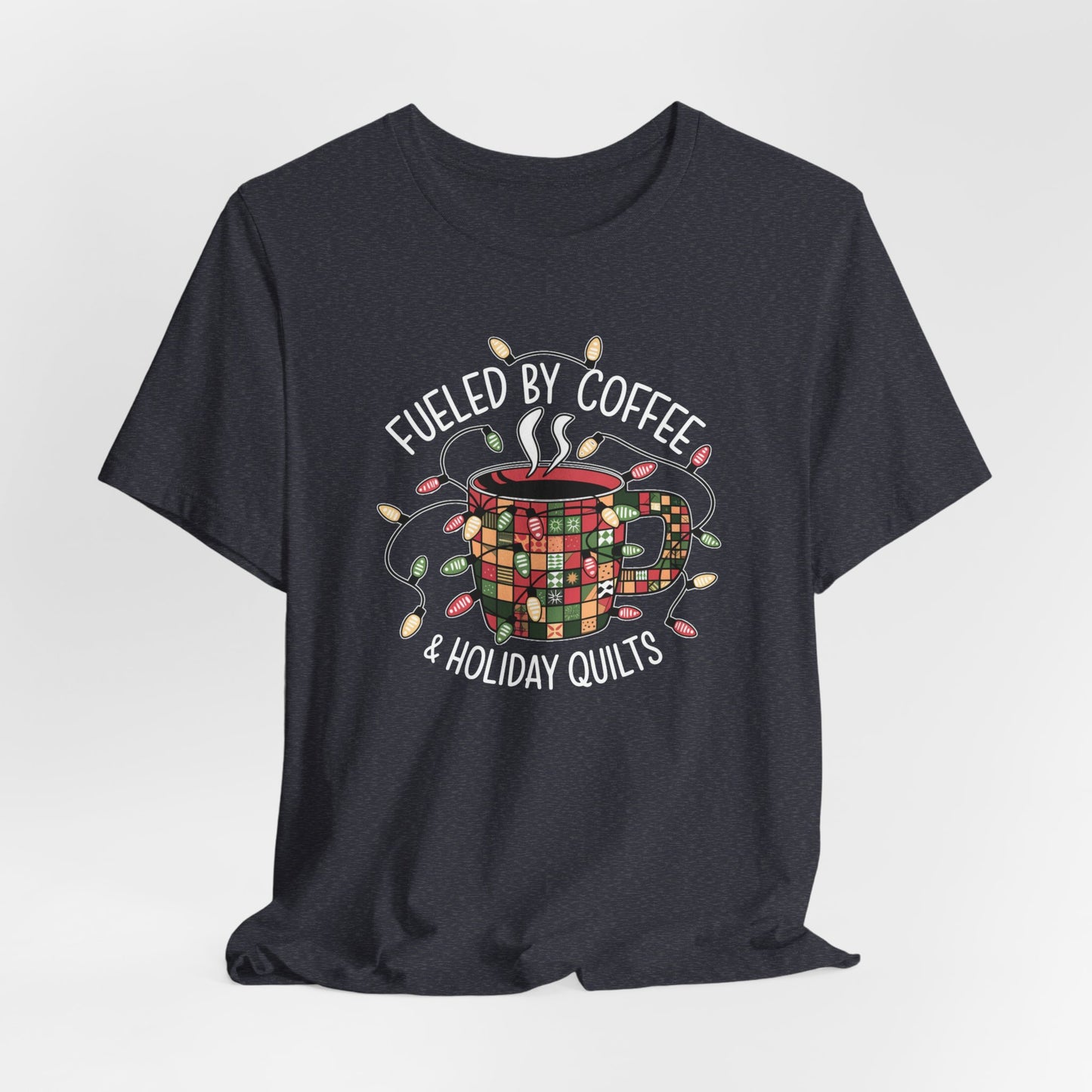 A Heather Navy christmas quilting t-shirt featuring a cozy coffee mug covered in patchwork quilt patterns, wrapped in festive holiday lights, with the phrase "Fueled by Coffee & Holiday Quilts" surrounding the design.