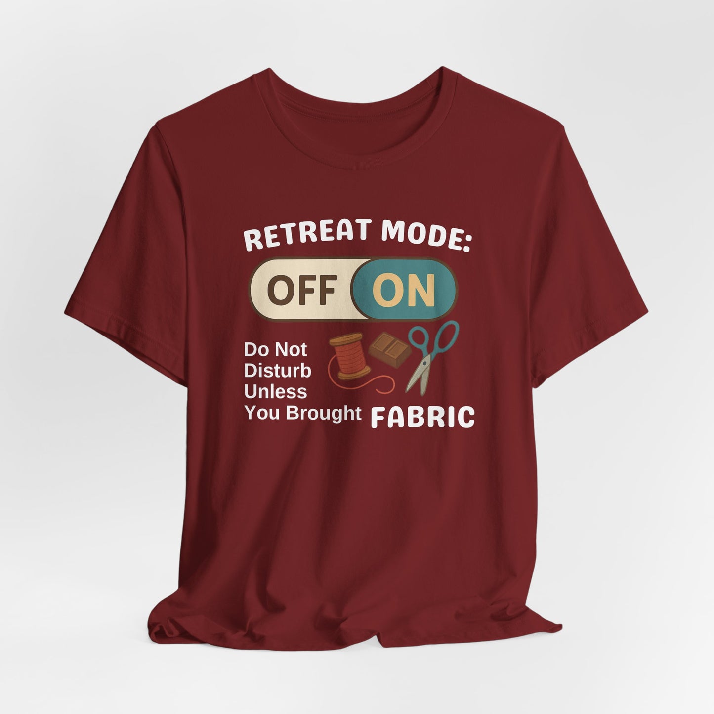A A Cardinal t-shirt with a toggle switch that says "Retreat Mode: OFF/ON" surrounded by a spool of thread, chocolate, and scissors. Text below reads "Do not disturb unless you brought fabric." Fun gift for quilting retreats.
