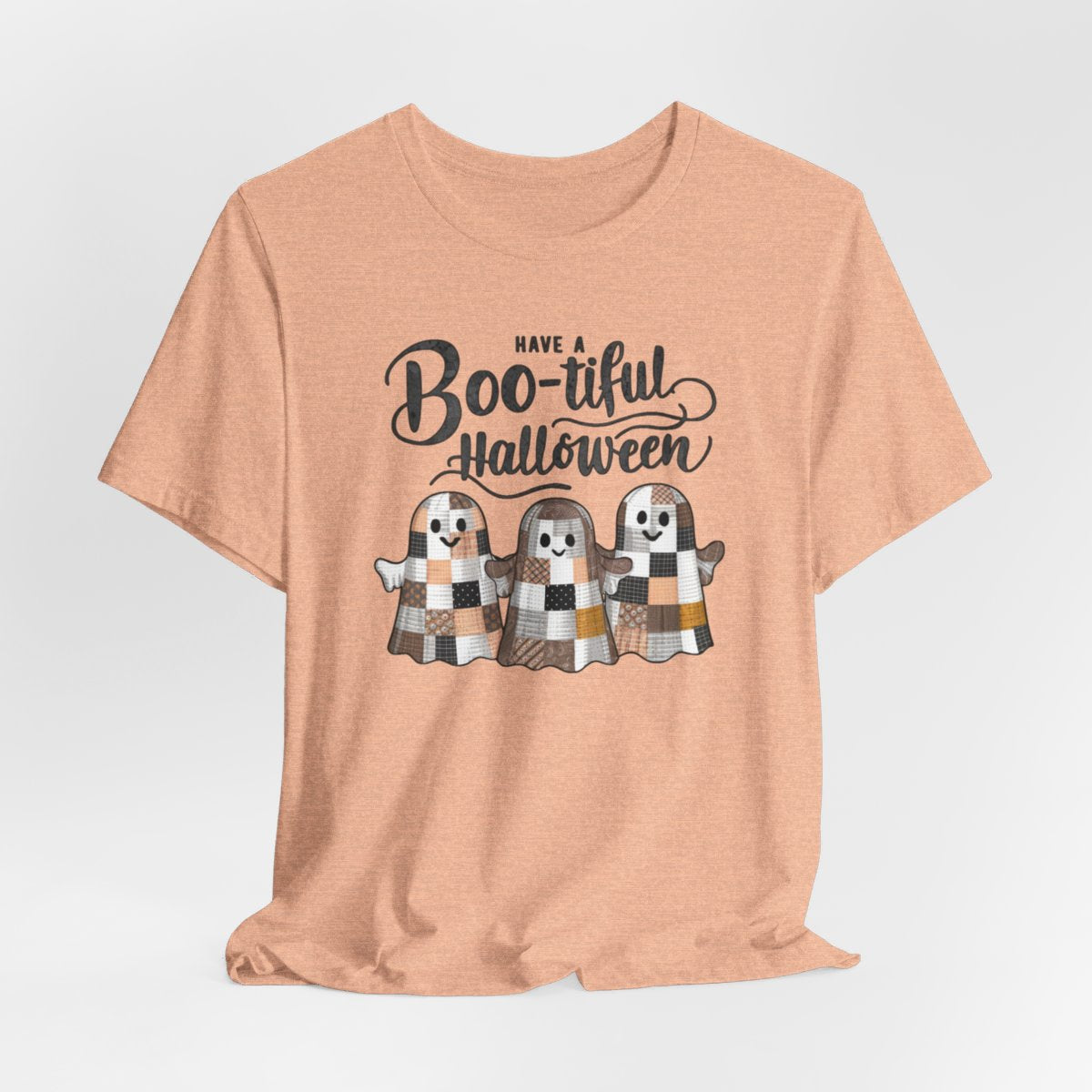 A Heather Peach Halloween Quilting T-Shirt featuring three smiling patchwork ghosts made of various quilt patterns in autumn colors. Text reads "Have a Boo-tiful Halloween" in stylized lettering. Perfect for quilters who love Halloween.