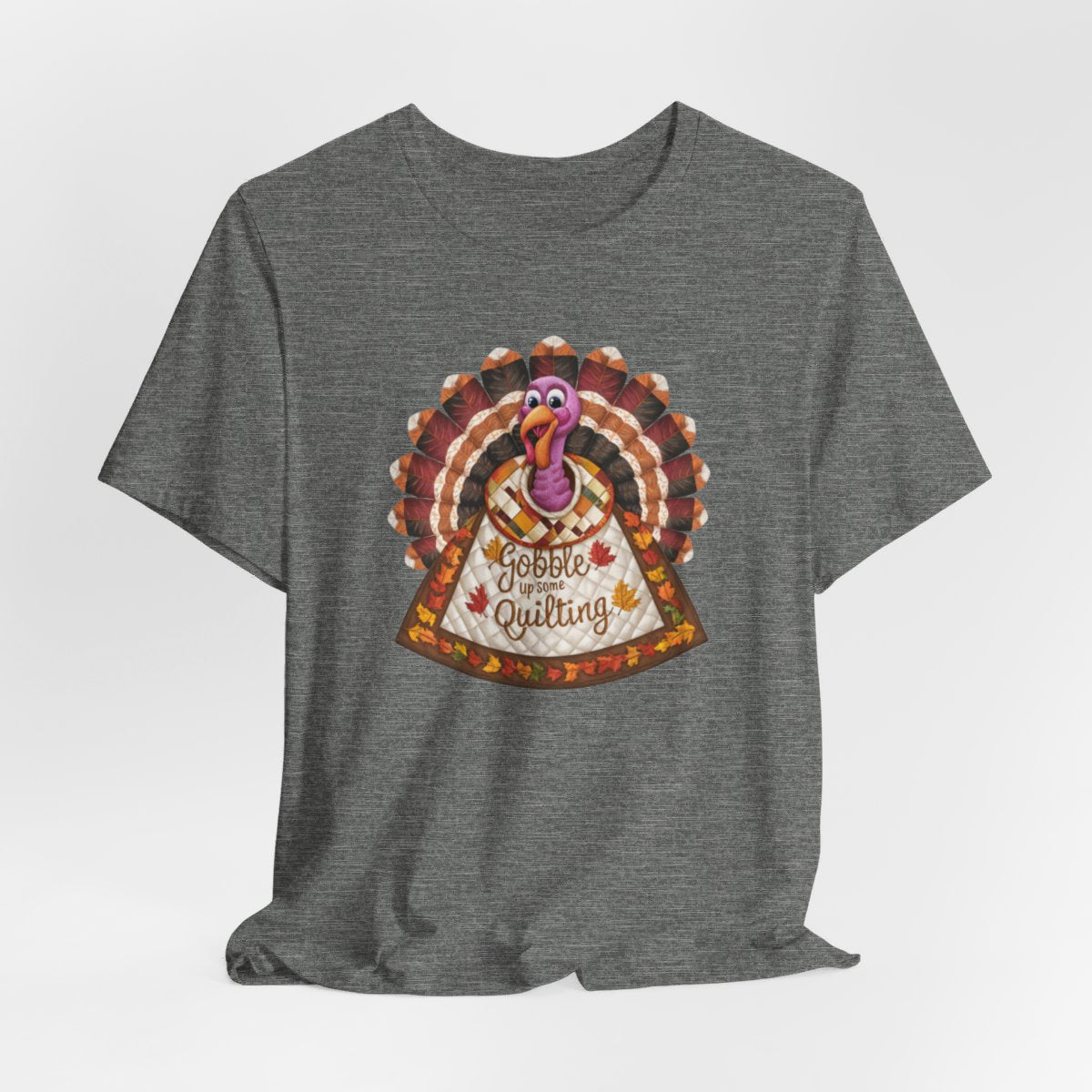 A Deep Heather thanksgiving quilting t-shirt featuring a quilted turkey design with colorful patchwork feathers and body. Text on turkey reads "Gobble up some Quilting" surrounded by fall leaves. Combines Thanksgiving imagery with quilting motifs in a whimsical illustration.