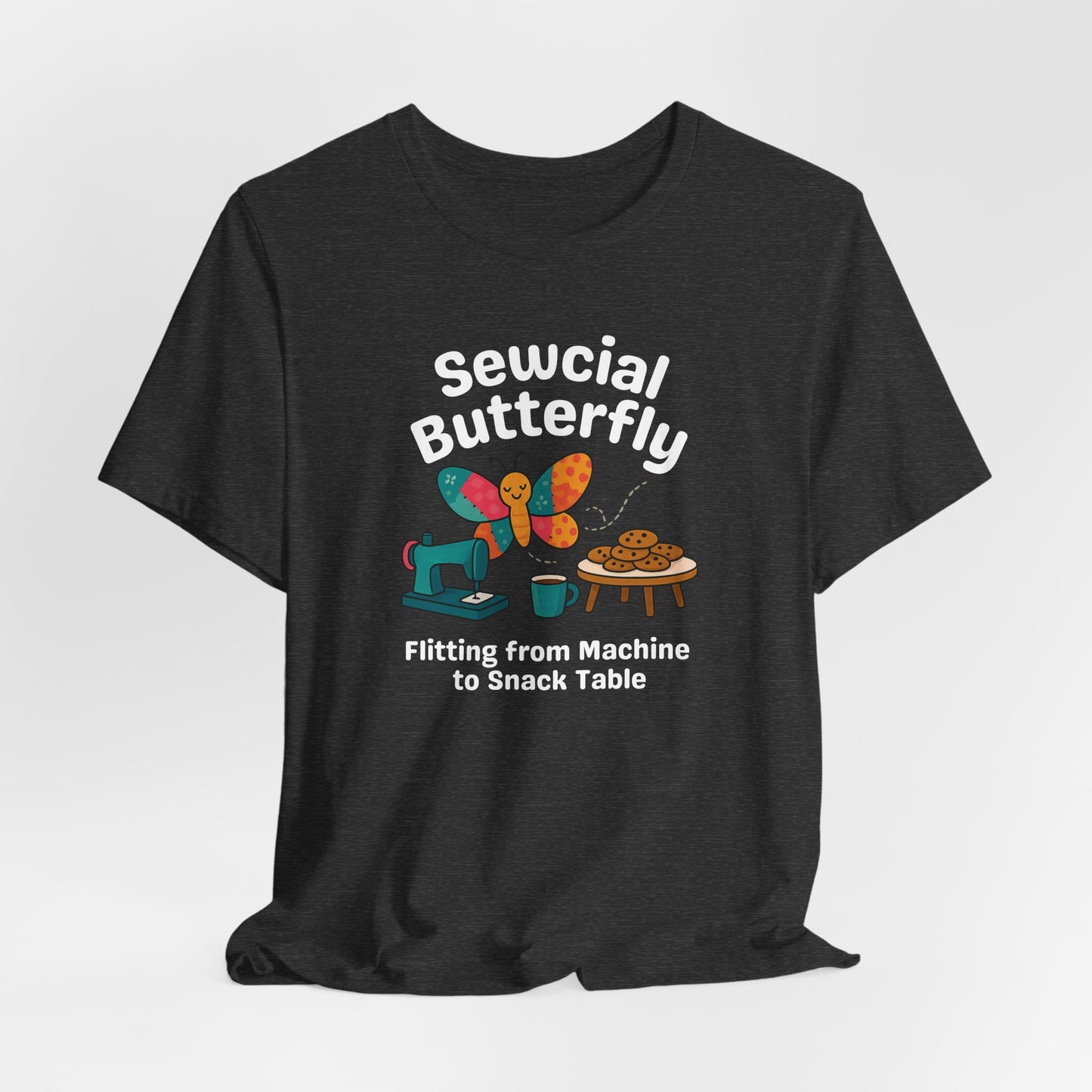 A A Dark Grey Heather t-shirt with a colorful design showing a patchwork butterfly flying between a sewing machine and a table of cookies. Text reads “Sewcial Butterfly – Flitting from Machine to Snack Table.” Funny gift for quilters
