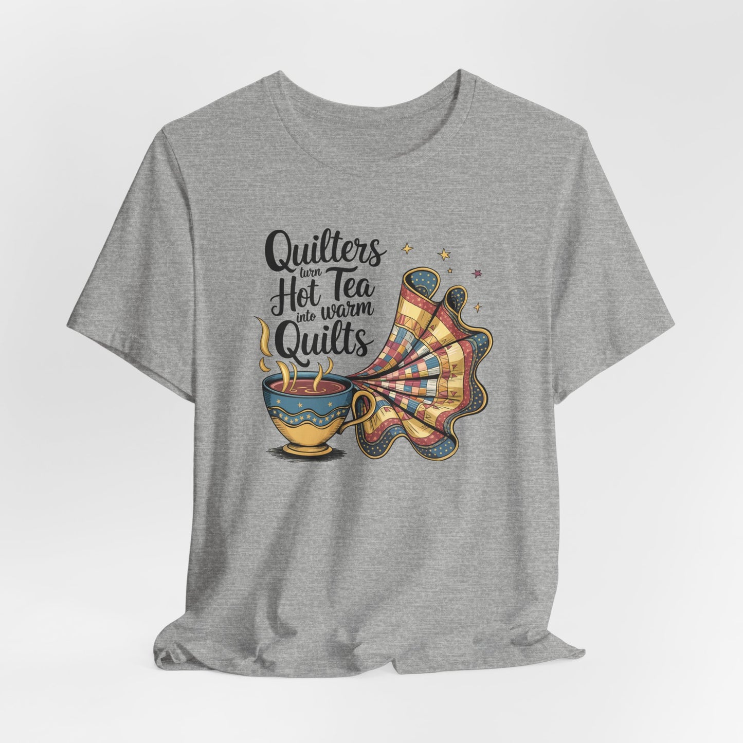An Athletic Heather t-shirt with a whimsical design of a teacup transforming into a patchwork quilt, accompanied by the phrase 'Quilters turn hot tea into warm quilts.' Ideal for quilters and tea lovers