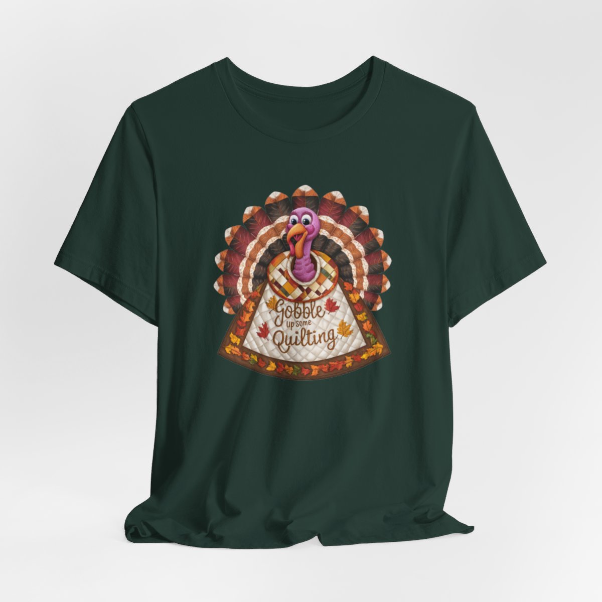 A Forest thanksgiving quilting t-shirt featuring a quilted turkey design with colorful patchwork feathers and body. Text on turkey reads "Gobble up some Quilting" surrounded by fall leaves. Combines Thanksgiving imagery with quilting motifs in a whimsical illustration.