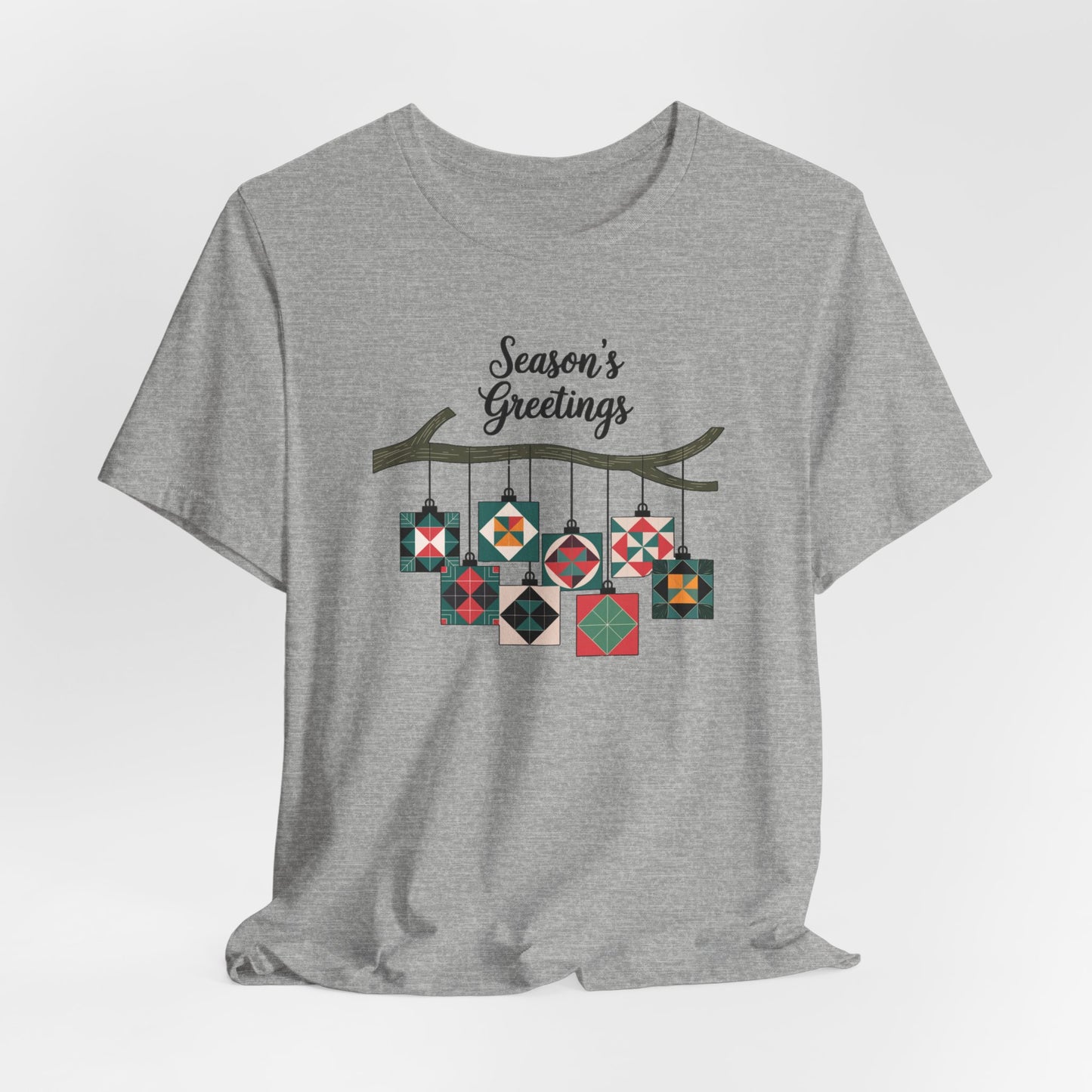 An Athletic Heather christmas quilting t-shirt featuring quilt block ornaments hanging from a branch, featuring the phrase "Season's Greetings" above. The ornaments showcase various quilting patterns to highlight the holiday quilting theme.