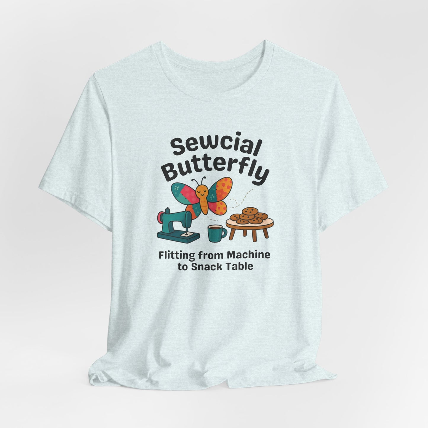 A A Heather Ice Blue t-shirt with a colorful design showing a patchwork butterfly flying between a sewing machine and a table of cookies. Text reads “Sewcial Butterfly – Flitting from Machine to Snack Table.” Funny gift for quilters