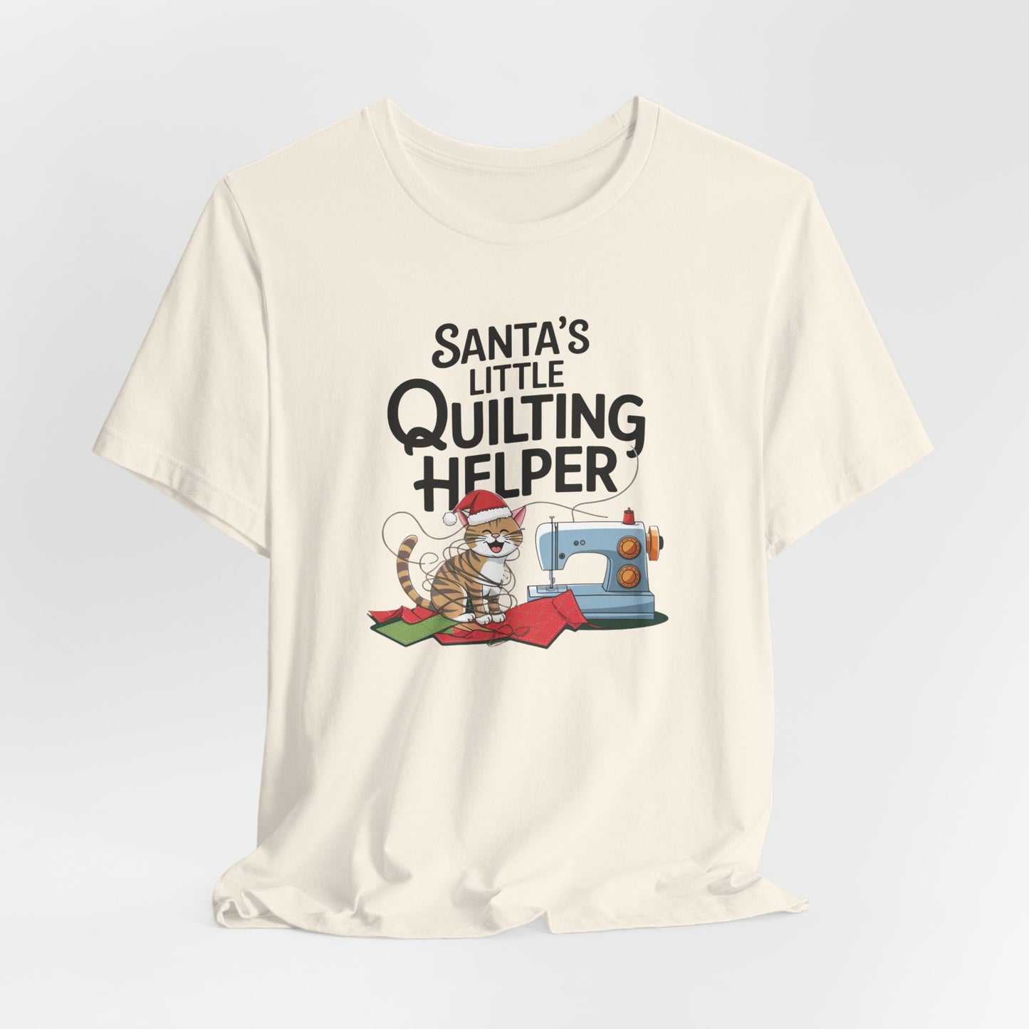 A Natural christmas quilting t-shirt featuring a playful cat wearing a Santa hat is tangled in thread next to a sewing machine, with the phrase "Santa's Little Quilting Helper" above, combining quilting and holiday humor.