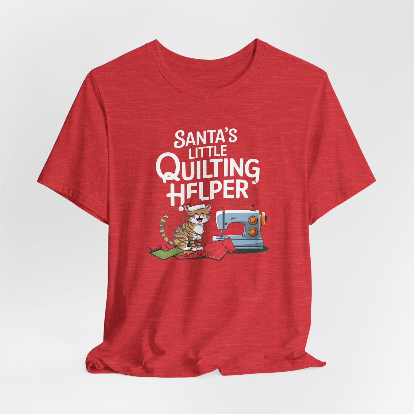A Heather Red christmas quilting t-shirt featuring a playful cat wearing a Santa hat is tangled in thread next to a sewing machine, with the phrase "Santa's Little Quilting Helper" above, combining quilting and holiday humor.
