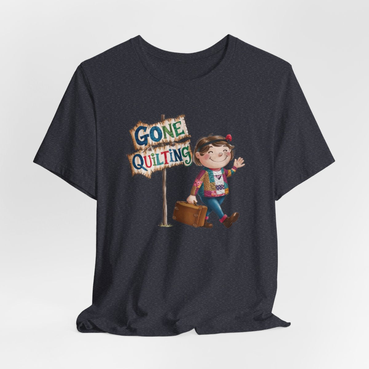 A Heather Navyfun quilting T-Shirt with a cartoon illustration of a smiling girl wearing a patchwork jacket, carrying a suitcase next to a wooden sign that reads "Gone Quilting" in colorful letters.