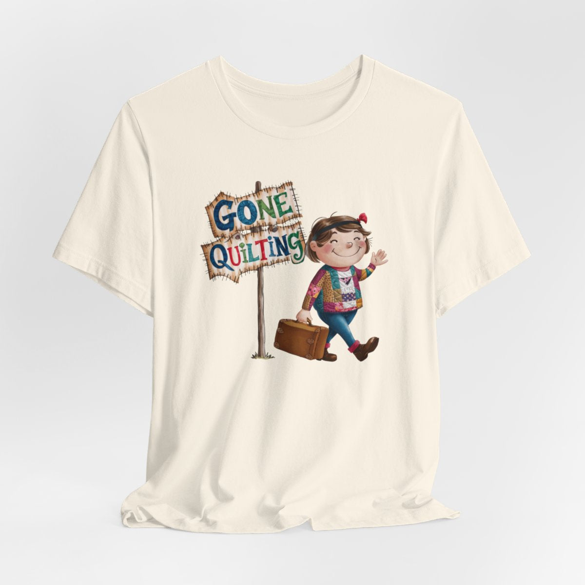 A Naturalfun quilting T-Shirt with a cartoon illustration of a smiling girl wearing a patchwork jacket, carrying a suitcase next to a wooden sign that reads "Gone Quilting" in colorful letters.