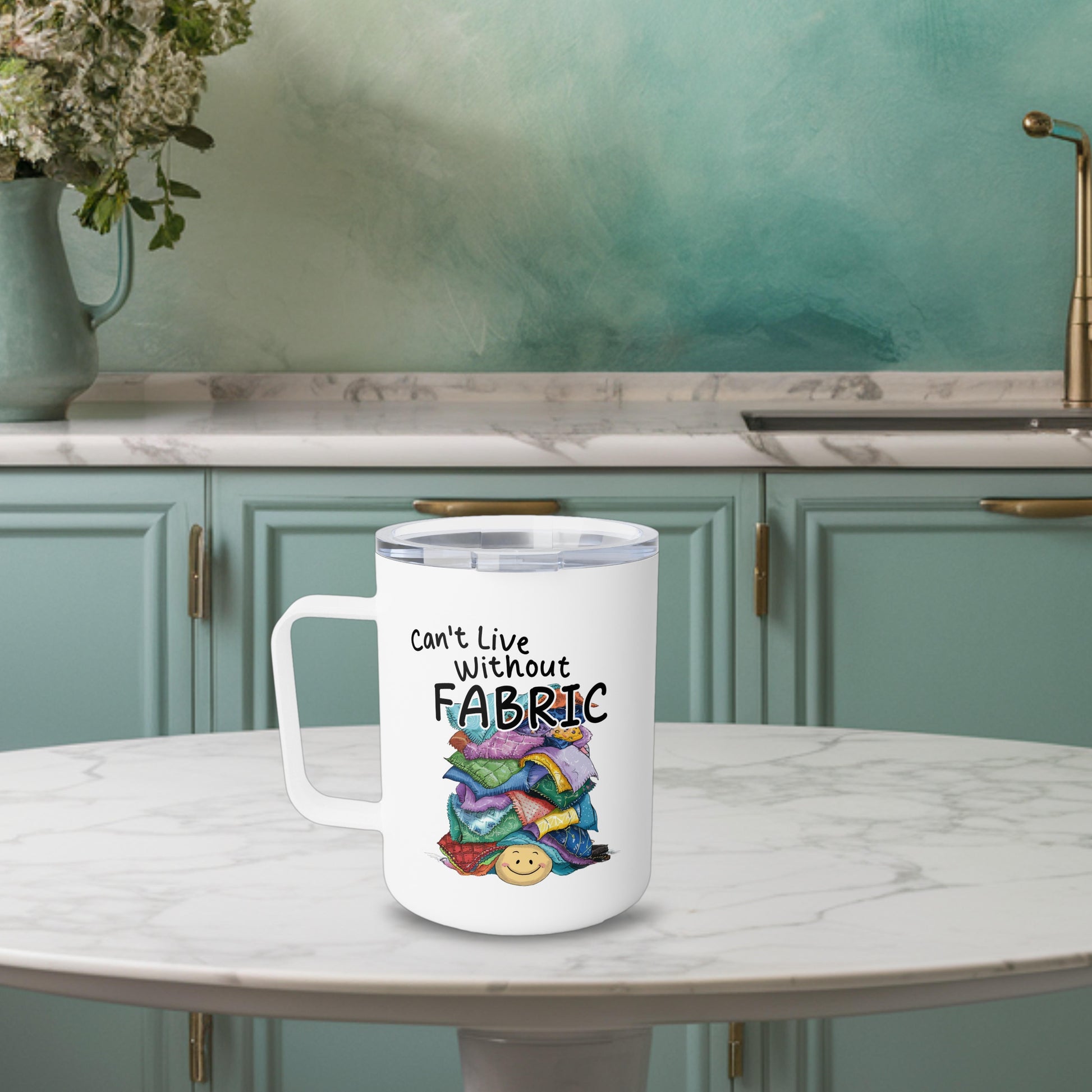 A funny quilting-inspired Insulated Mug with an Illustration of a smiling face underneath a pile of colorful fabric scraps. Text reads "Can't Live Without Fabric" in a handwritten style. The fabrics feature various patterns and textures in multiple colors.