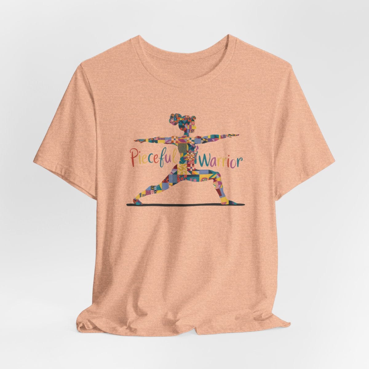 A Heather Peach Tee featuring a colorful patchwork silhouette of woman in yoga warrior pose. Text reads "Pieceful Warrior" in multicolored lettering.