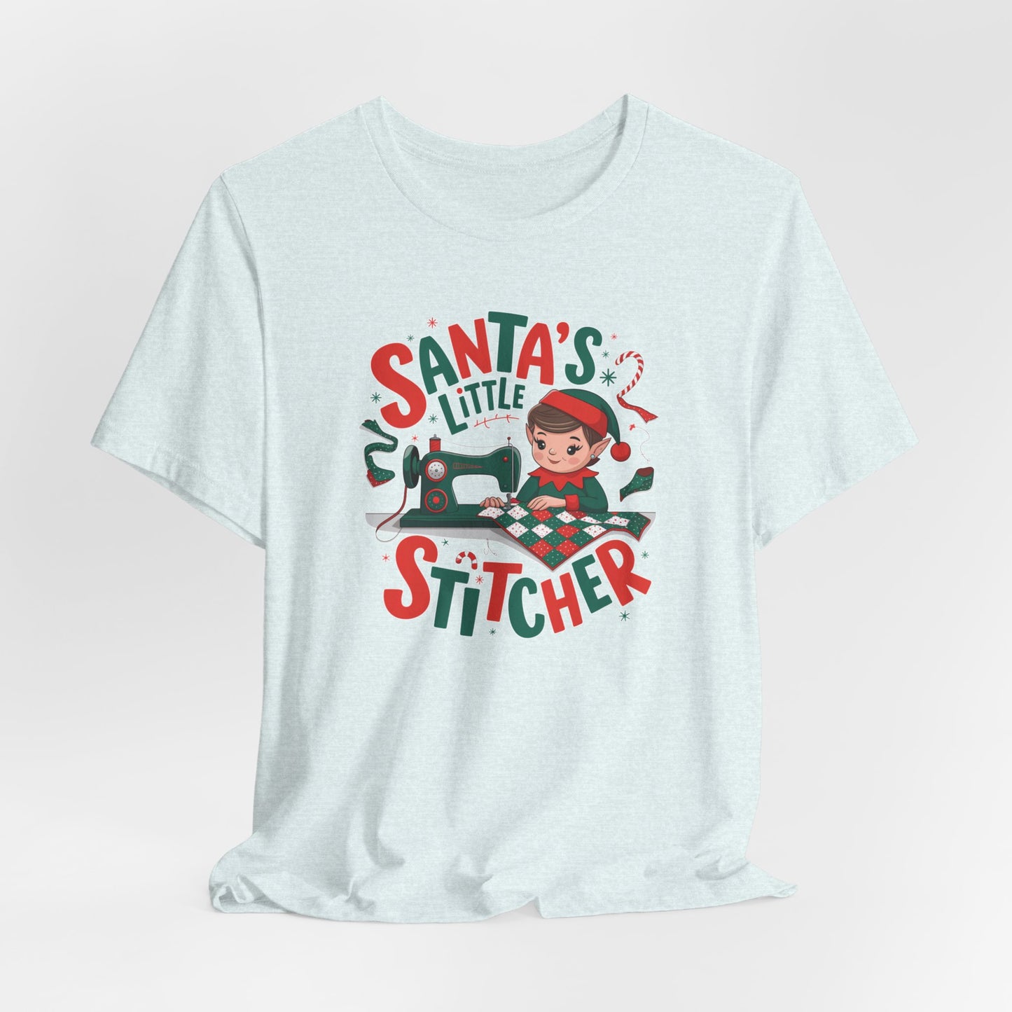 A Heather Ice Blue christmas quilting t-shirt featuring an adorable elf is sewing a festive patchwork quilt on a sewing machine, surrounded by holiday-themed decorations, with the phrase "Santa's Little Stitcher" above and below the design.