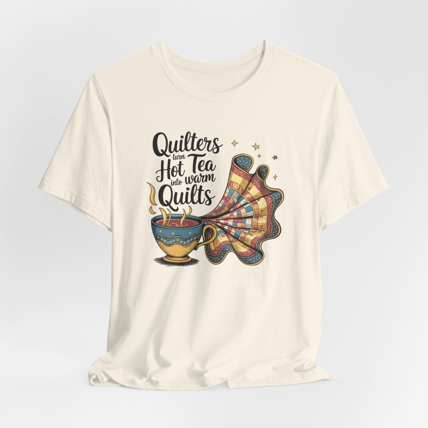 A Natural t-shirt with a whimsical design of a teacup transforming into a patchwork quilt, accompanied by the phrase 'Quilters turn hot tea into warm quilts.' Ideal for quilters and tea lovers