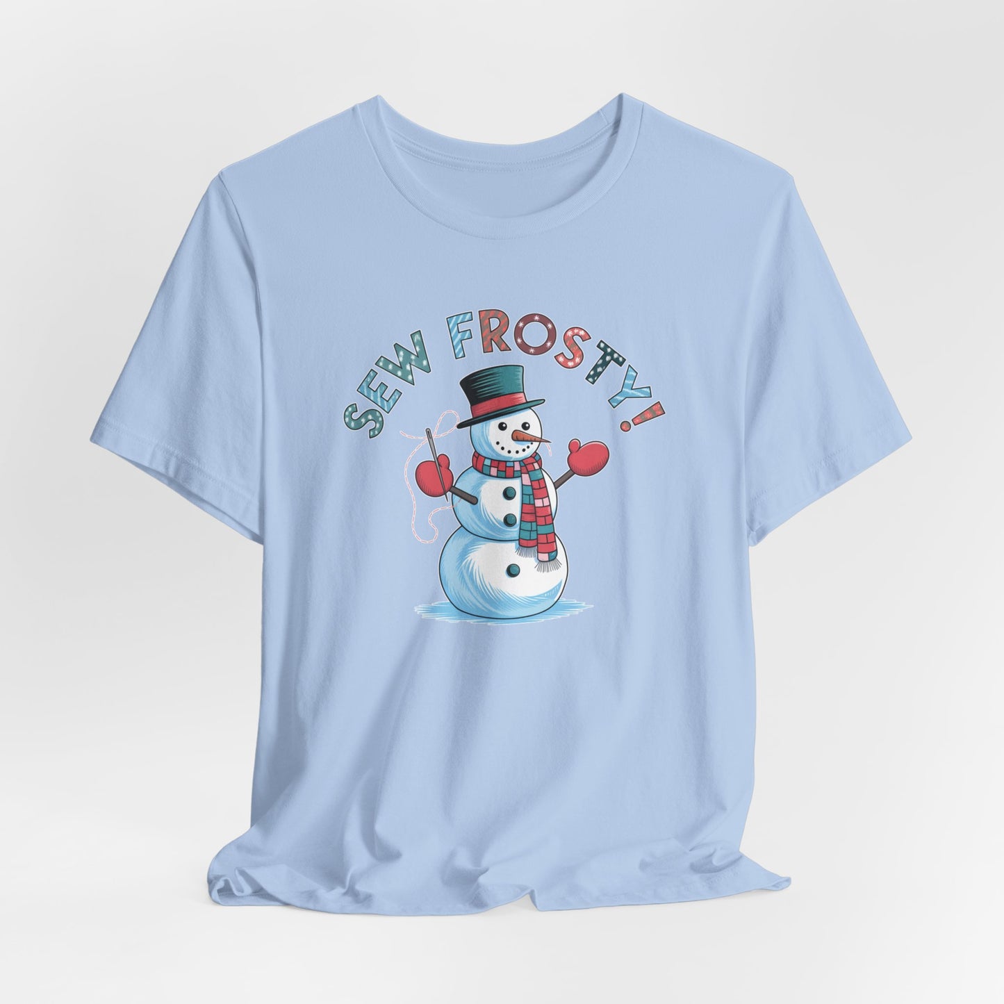 A Baby Blue christmas quilting t-shirt featuring cheerful snowman design holding a sewing needle, with the phrase "Sew Frosty" in playful, winter-themed lettering. The snowman is wearing a scarf and mittens, ready for holiday sewing fun.