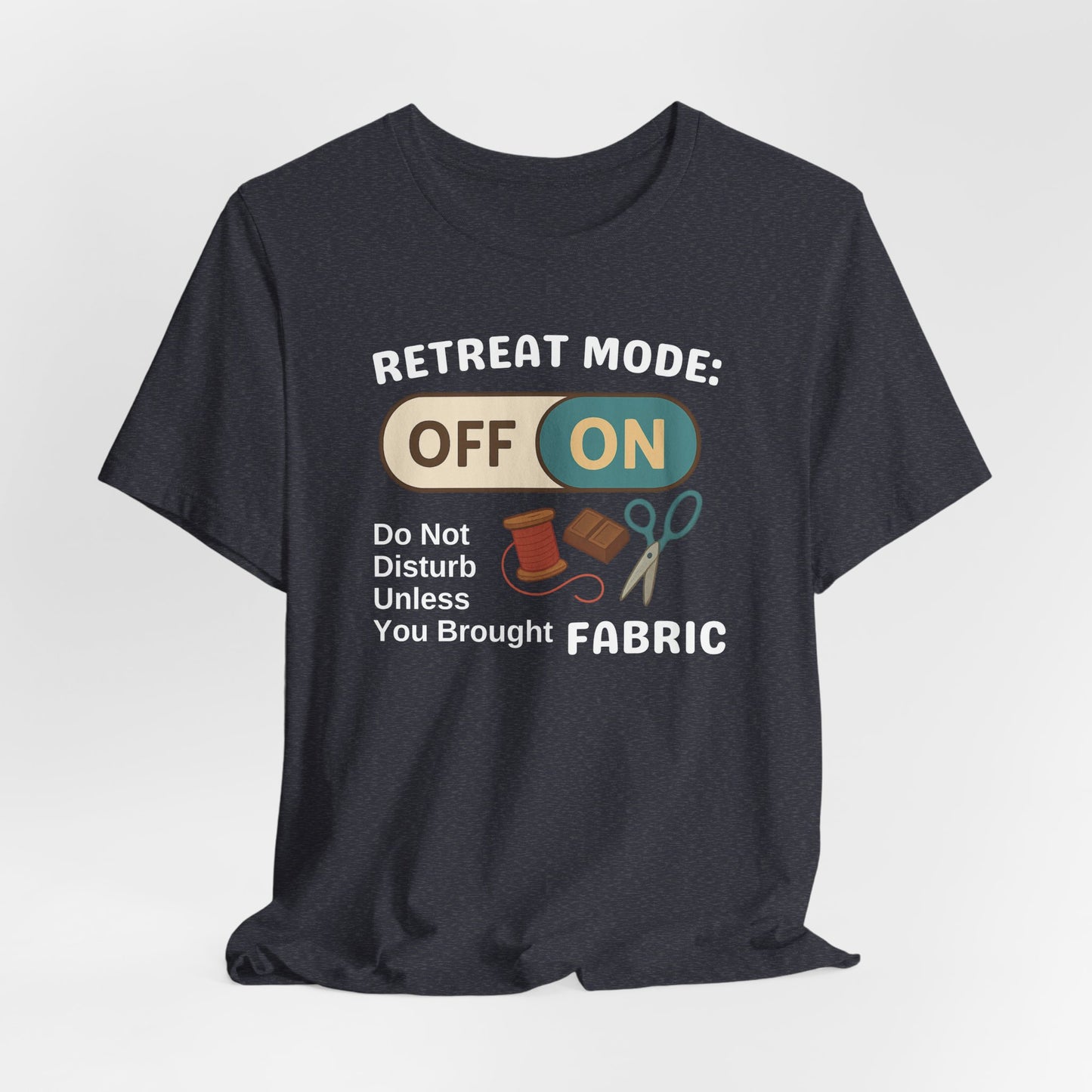 A A Heather Navy t-shirt with a toggle switch that says "Retreat Mode: OFF/ON" surrounded by a spool of thread, chocolate, and scissors. Text below reads "Do not disturb unless you brought fabric." Fun gift for quilting retreats.