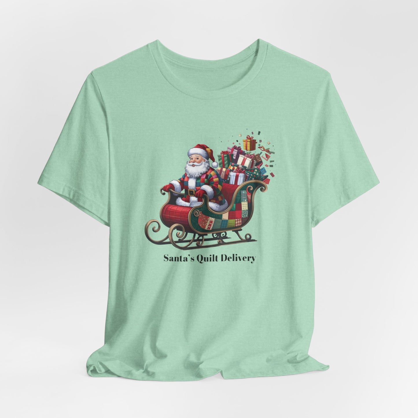 A Heather Mint christmas quilting t-shirt featuring Santa Claus wearing a patchwork quilt coat, sitting in a sleigh filled with gifts and quilts, with the phrase "Santa's Quilt Delivery" below, combining holiday cheer and quilting fun.