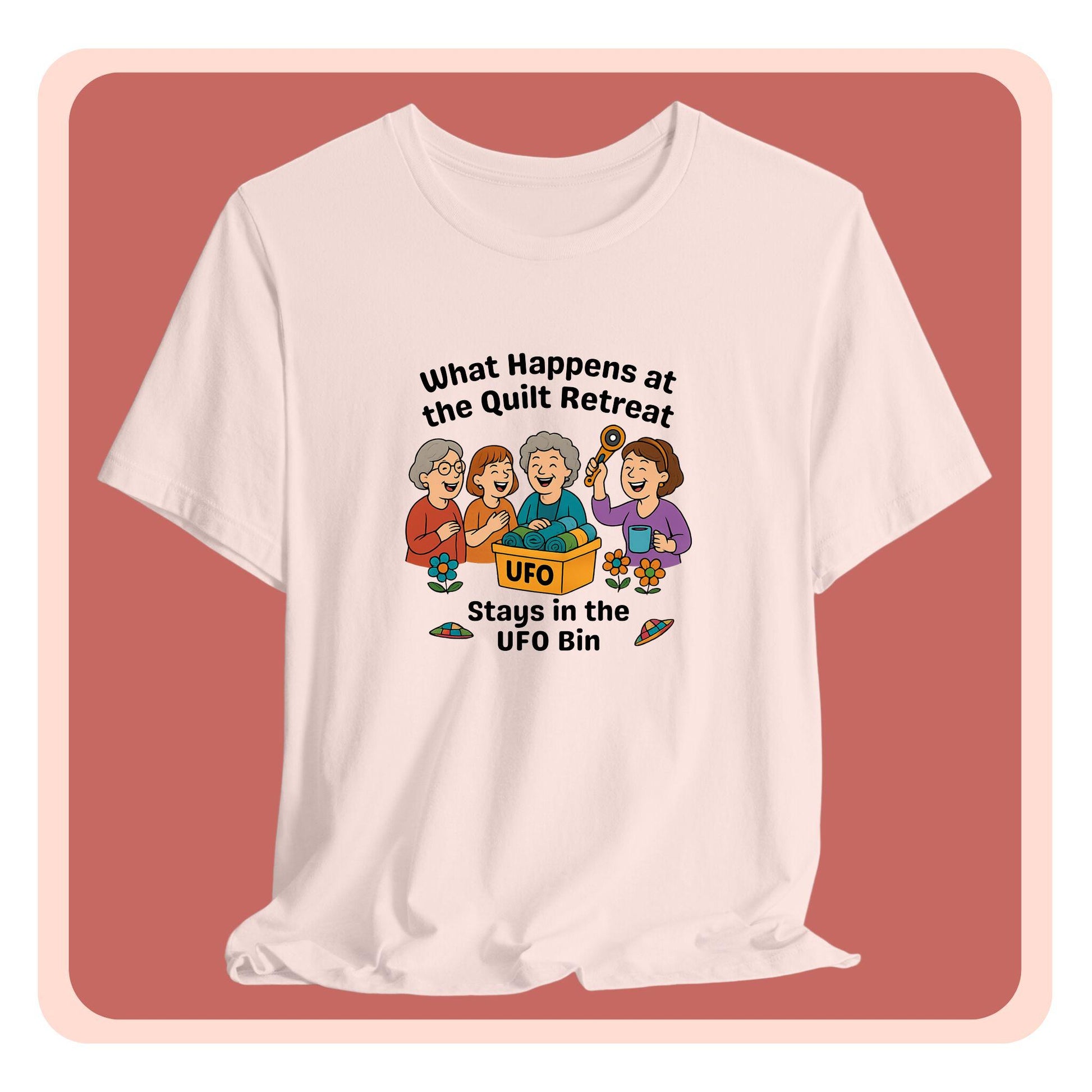 A A t-shirt featuring a cartoon design of four laughing women at a quilt retreat with a bin labeled “UFO” full of fabric. Surrounded by patchwork flying saucers and flowers. Text reads “What happens at the quilt retreat stays in the UFO bin.”